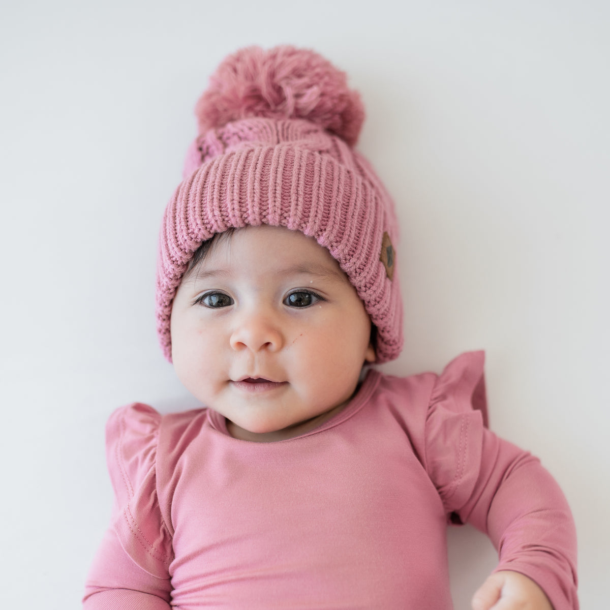 Close up of the Chunky Cable Knit Beanie in Apple Blossom shown on an infant wearing a matching long sleeve twirl bodysuit dress