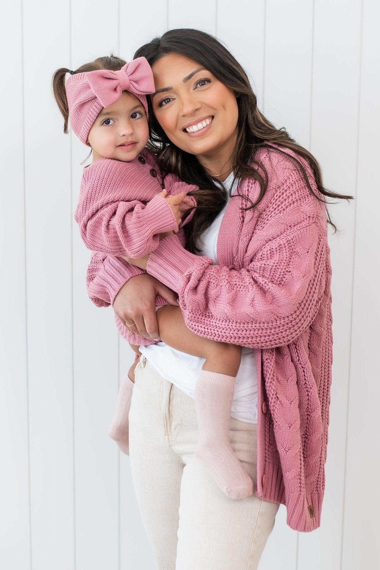 Smiling mother wearing the Cable Knit Adult Cardigan in Apple Blossom matching her daughter who is wearing a chunky knit romper in apple blossom