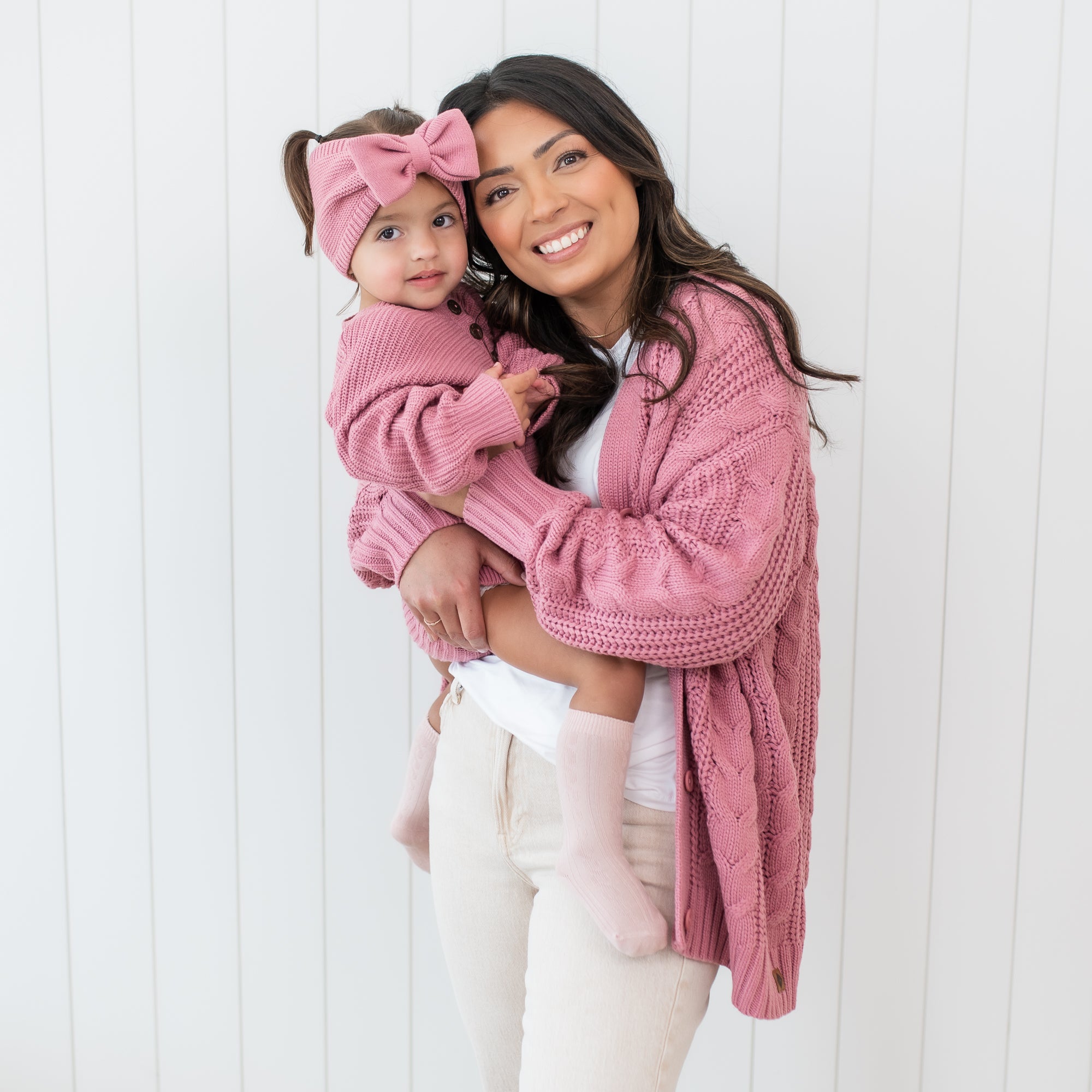 Smiling mother wearing the Cable Knit Adult Cardigan in Apple Blossom matching her daughter who is wearing a chunky knit romper in apple blossom
