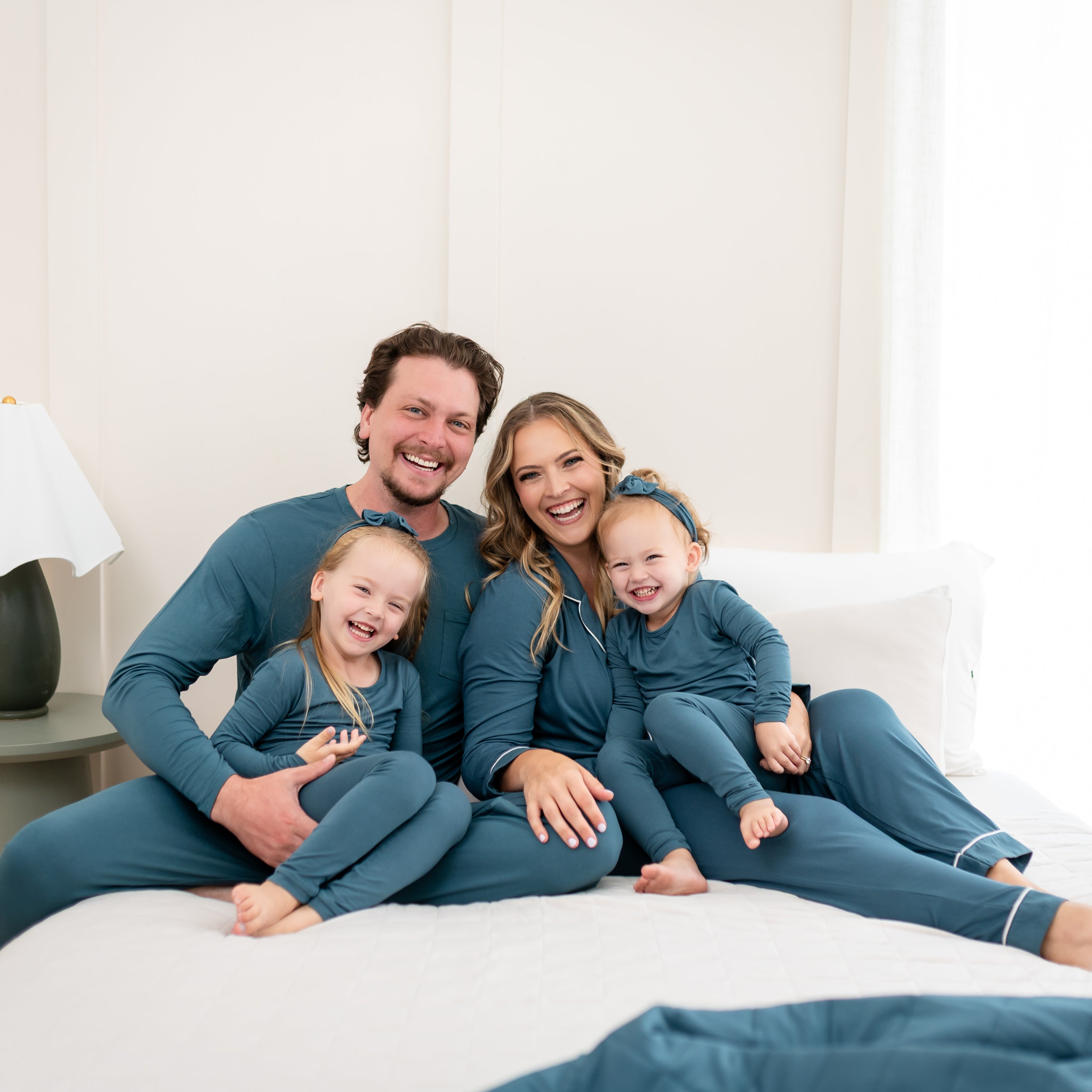 Family sitting on a bed all matching in Atlantic. Pictured is the Men's Jogger Set in Atlantic, Women's Long Sleeve Pajama Set and Long Sleeve Toddler pajamas