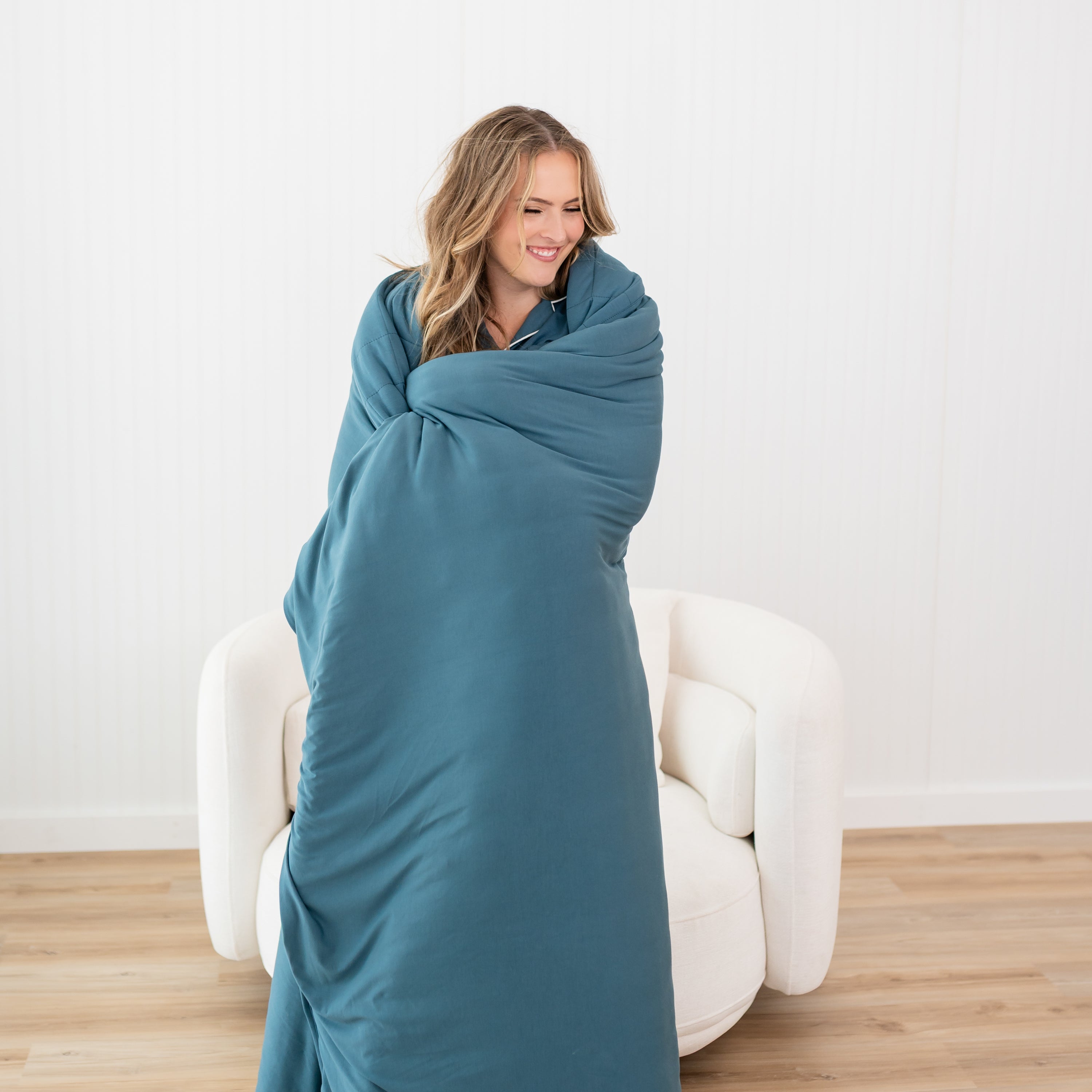 Smiling female standing wrapped in the Adult Quilted Blanket in Atlantic 2.5