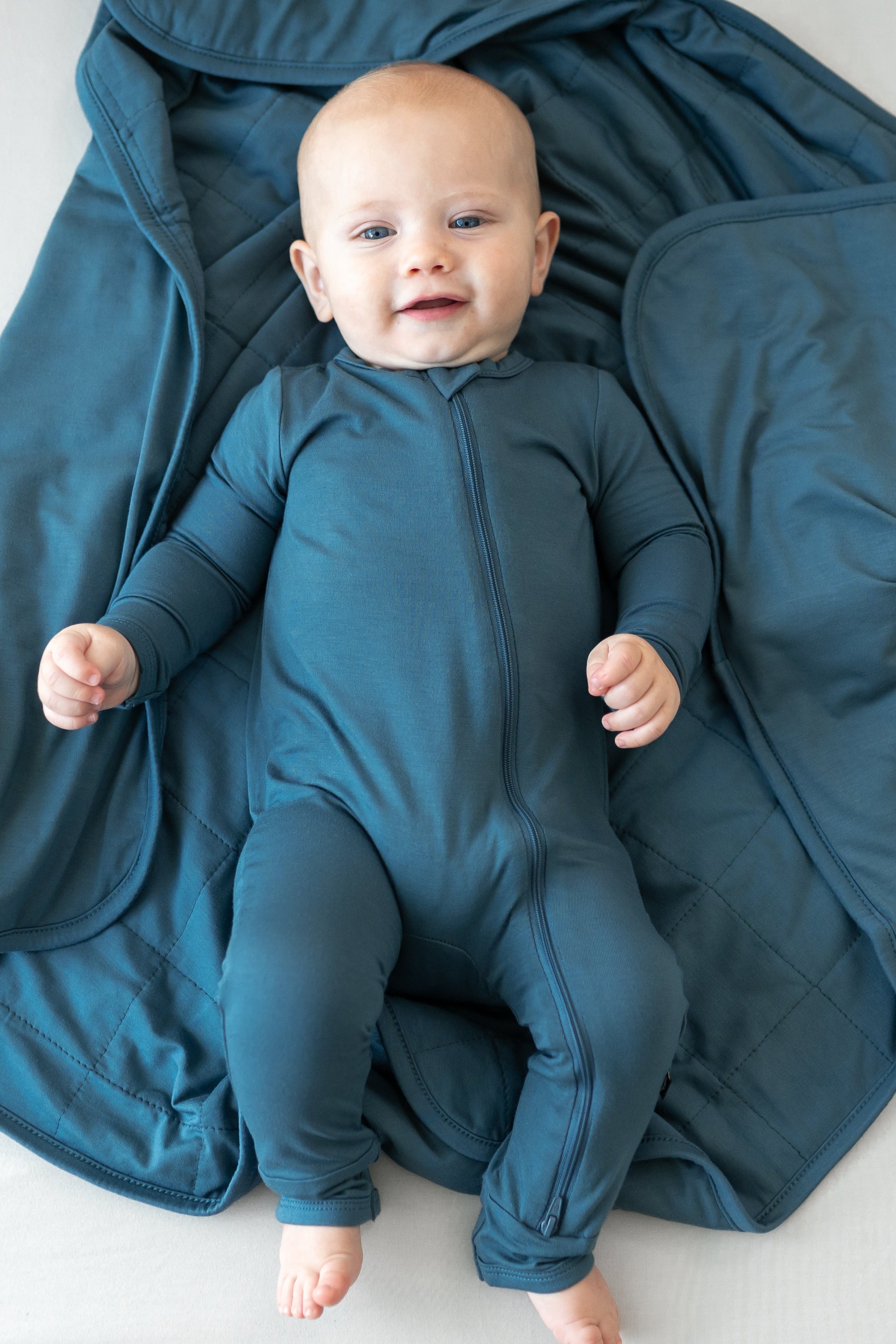 Infant laying on blue Baby Blanket in Atlantic TOG 1.0 wearing matching zippered romper pajamas