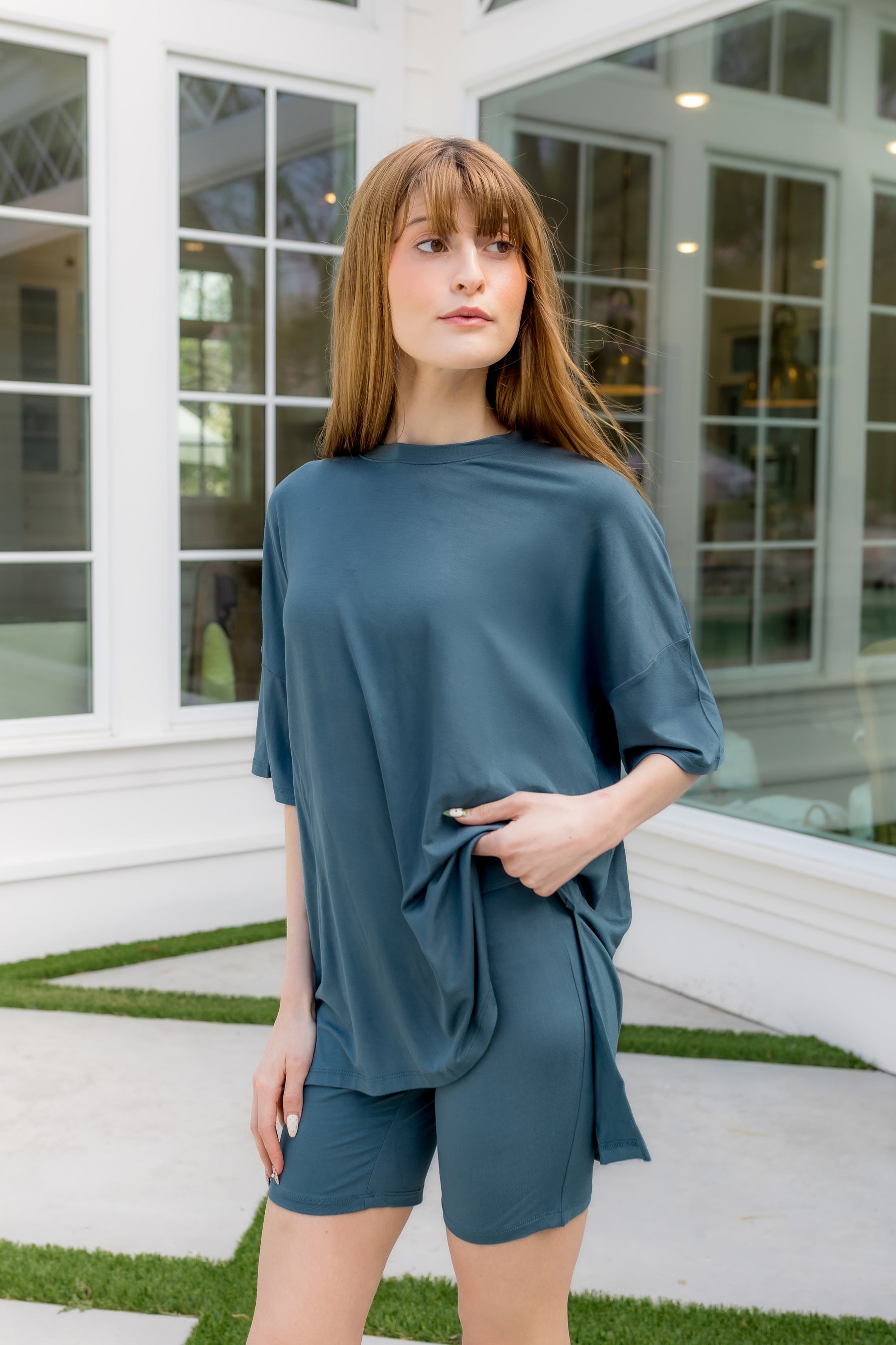 Female model standing in front of a white house wearing the Women’s Biker Short Set in Atlantic