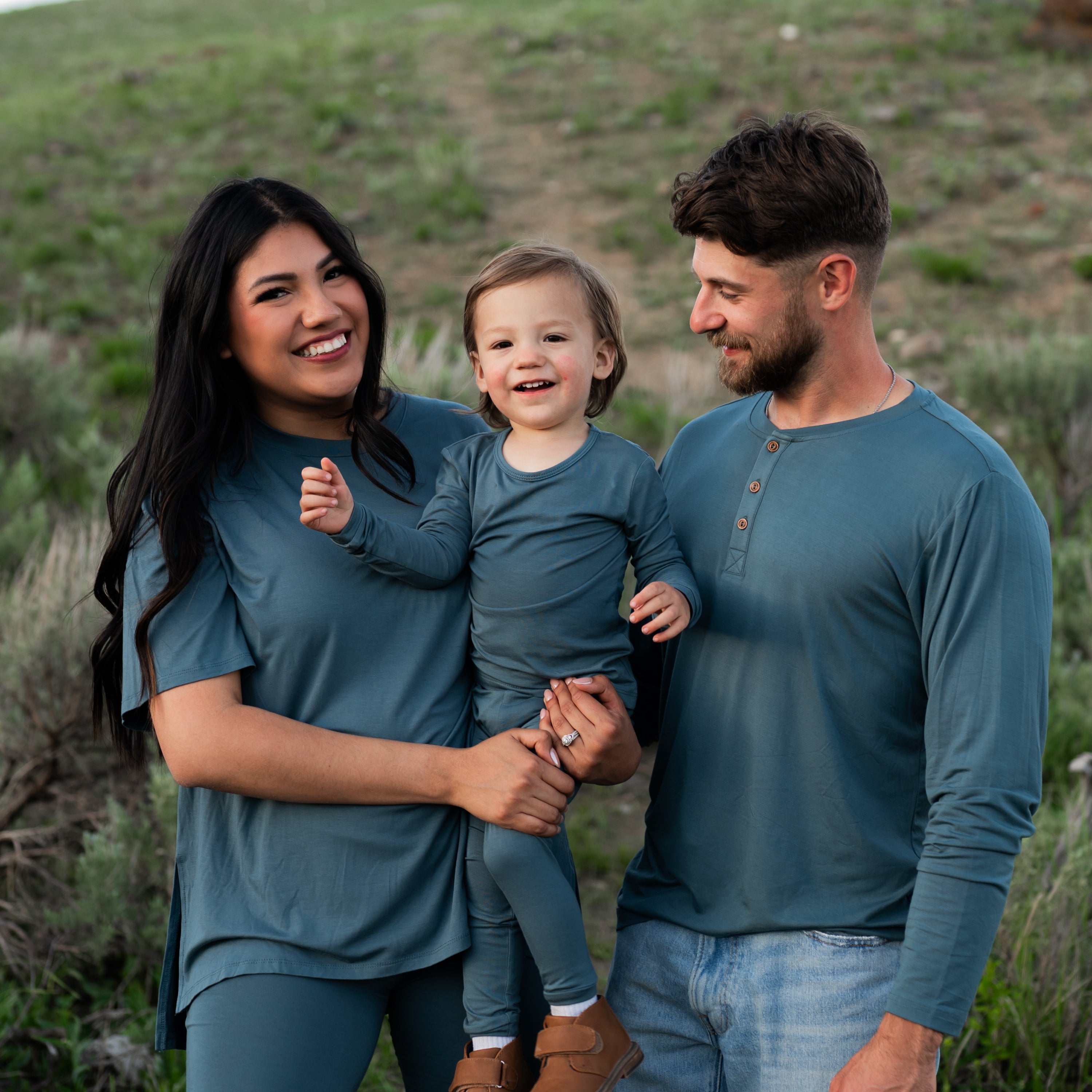 Family matching in Atlantic. Mother wearing Women's Biker Short Set, toddler wearing the Long Sleeve Pajamas in Atlantic and father wearing the Men's Long Sleeve Henley Tee