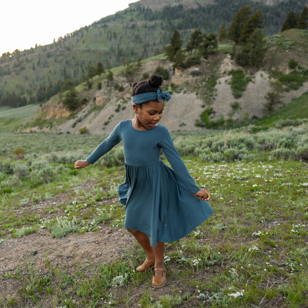 Girl twirling in a field wearing the Long Sleeve Twirl Dress in Atlantic paired with a matching bow headband