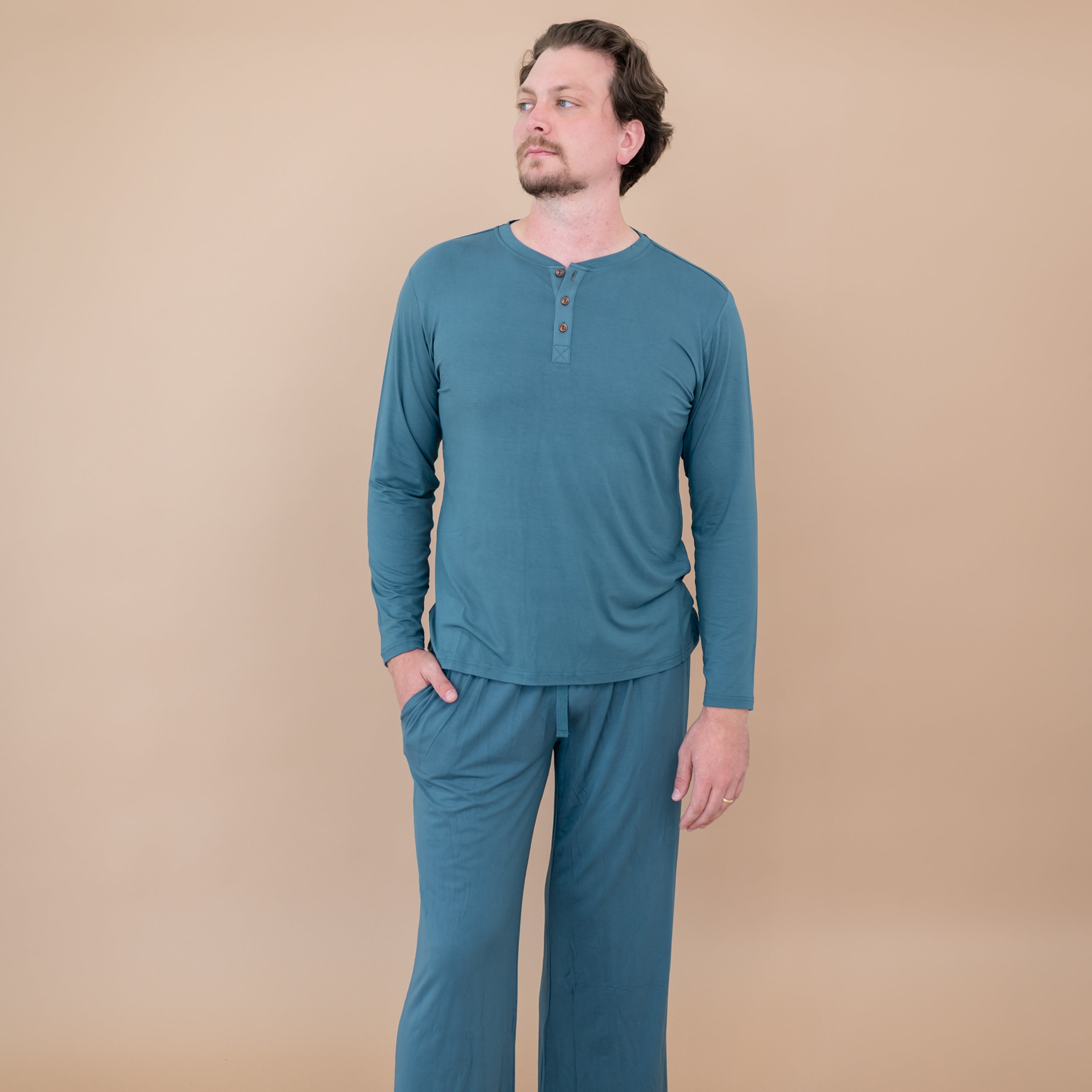 Male model standing with one hand in the pants pocket of the Men's Lounge Pants in Atlantic wearing a matching Men's Long Sleeve Henley top