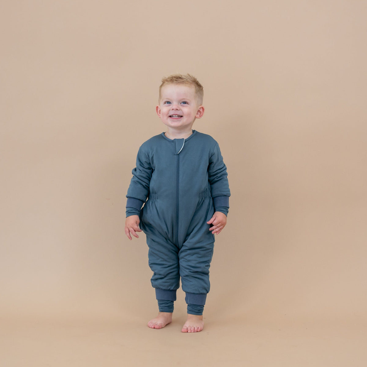 Toddler standing in front of a light taupe backdrop wearing the Cozy Playsuit in Atlantic