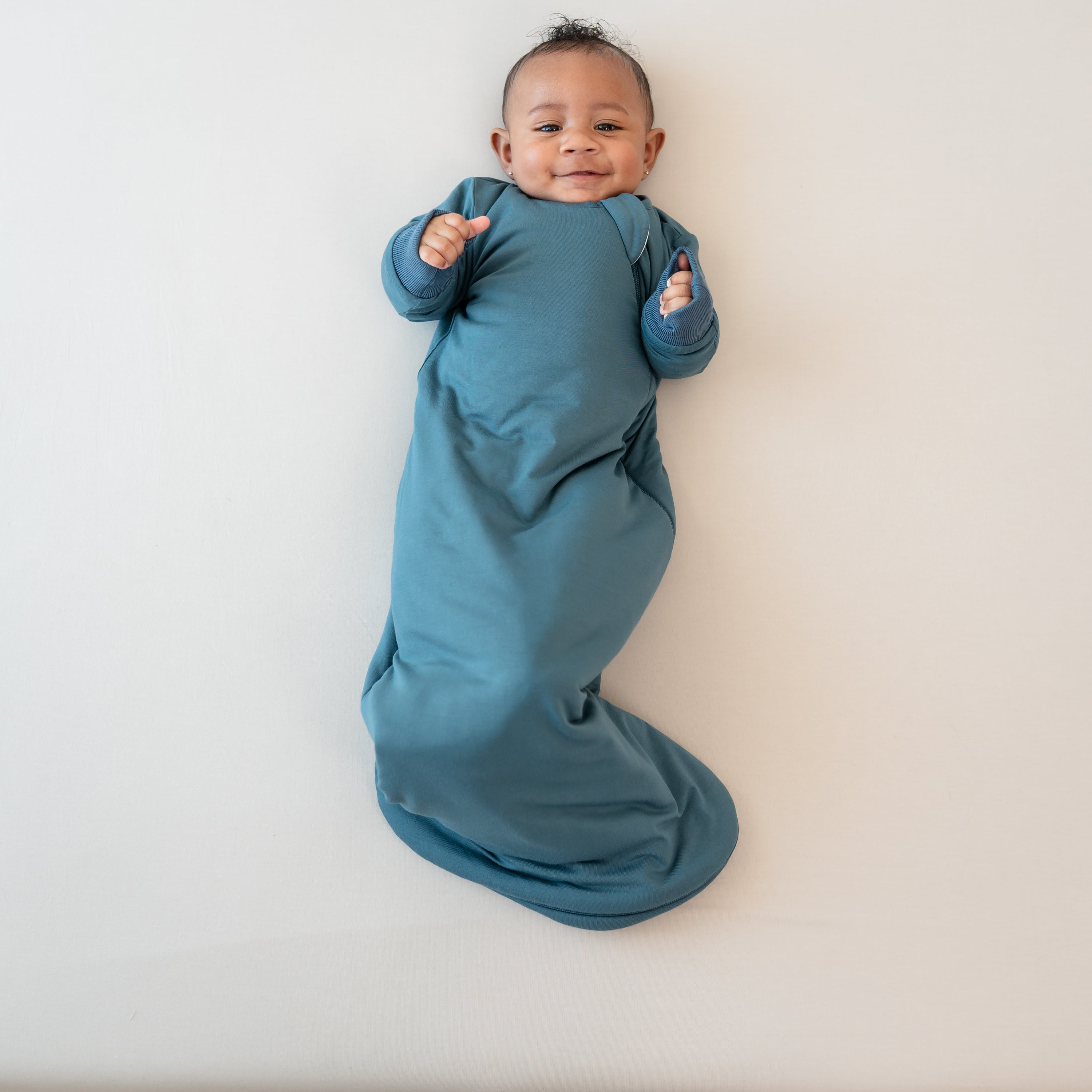 Smiling infant laying down with her hands in the air wearing the Slumber Bag in Atlantic