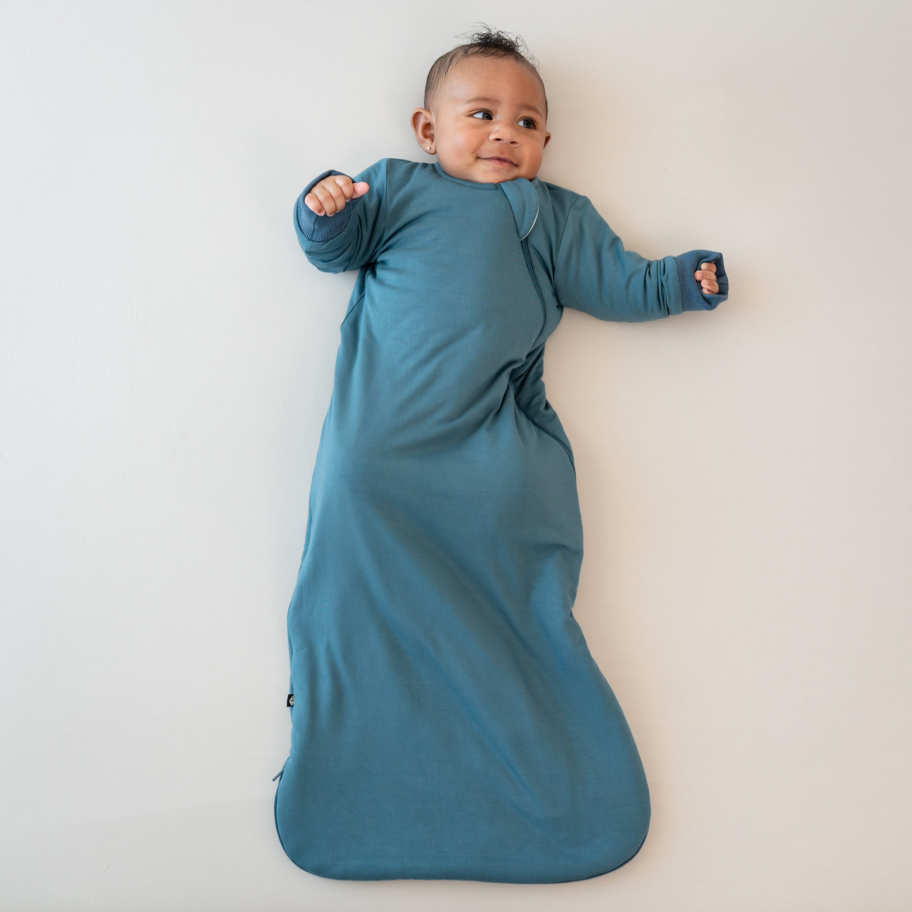 Infant laying down looking off to the side wearing the Slumber Bag in Atlantic