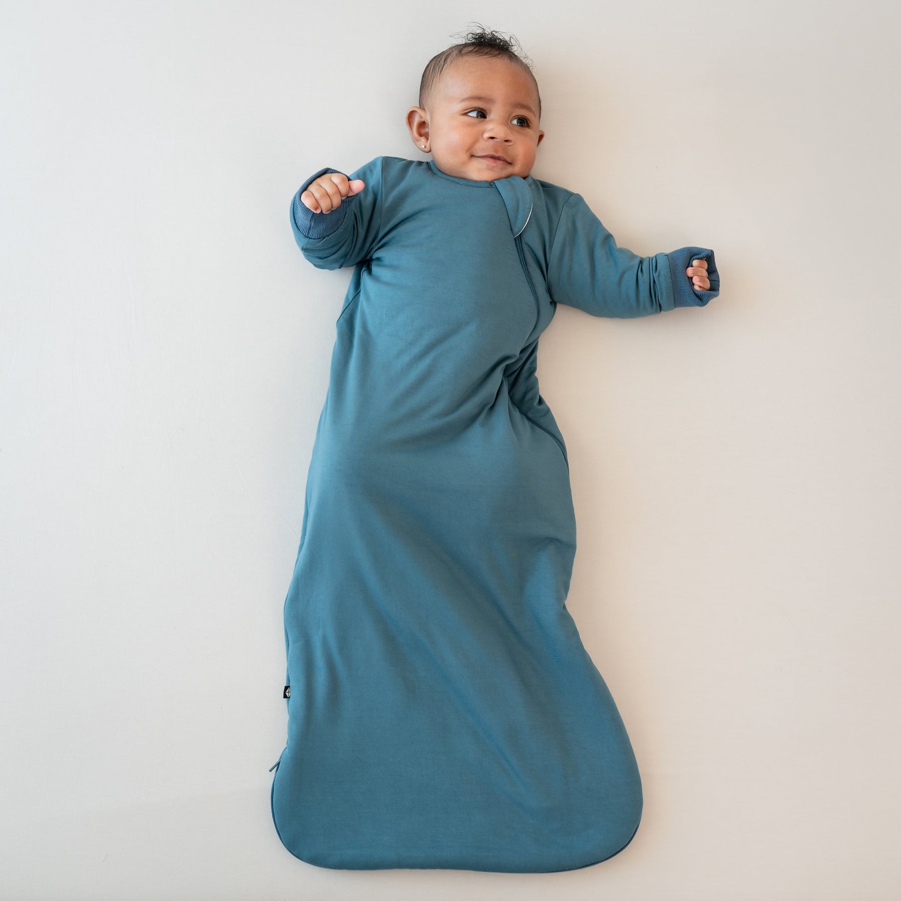 Infant laying down looking off to the side wearing the Slumber Bag in Atlantic