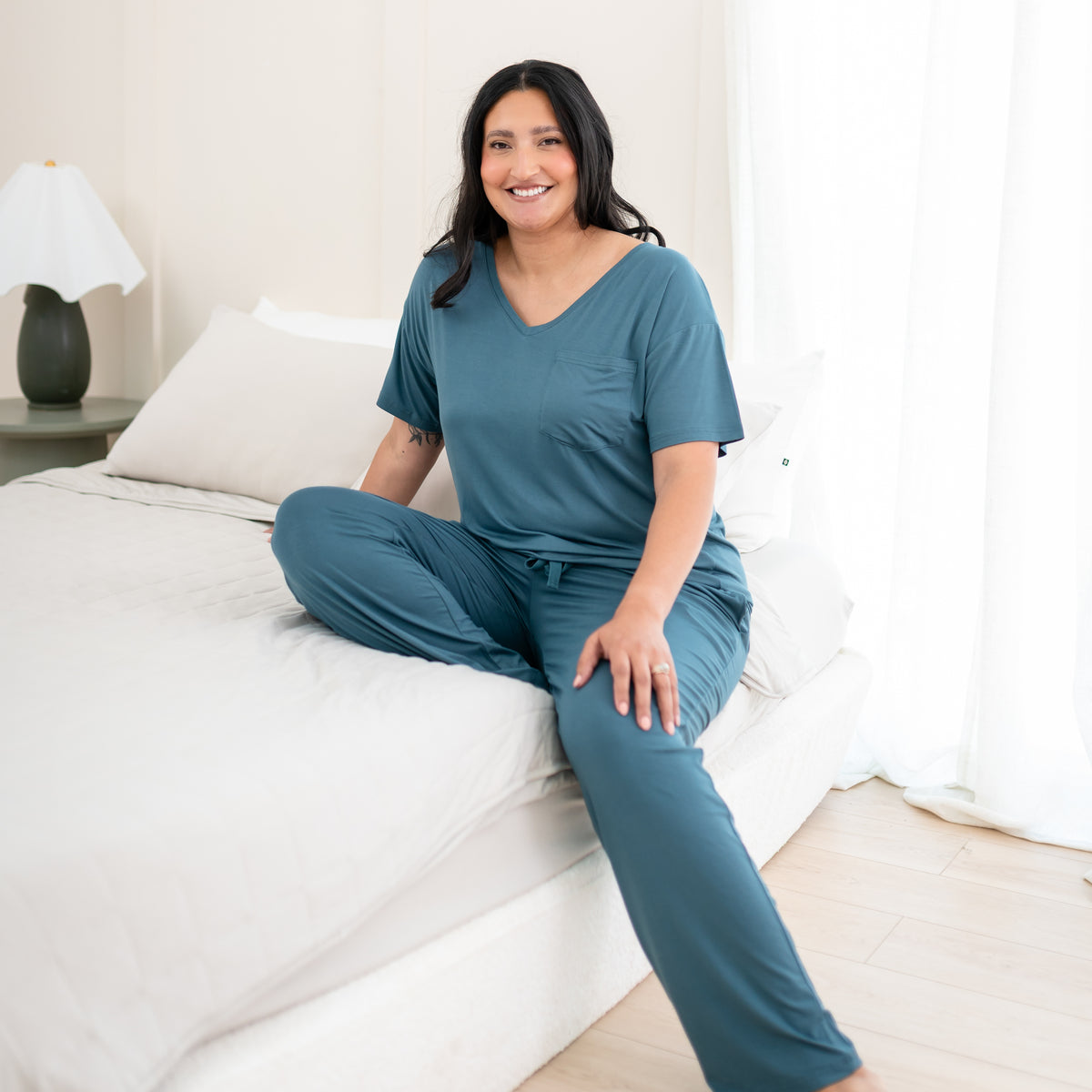 Female model sitting on a bed wearing the Women's Lounge Pants in Atlantic with matching women's v-neck