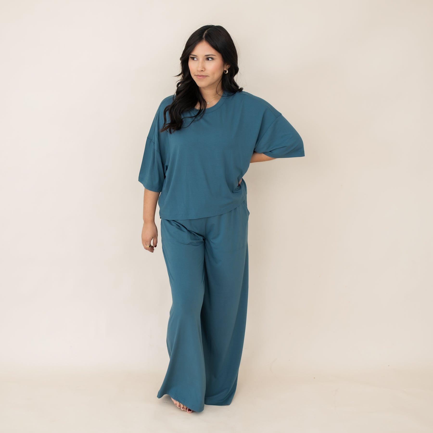 Smiling female standing in front of a light neutral background wearing the Women's Wide Leg Pant in Atlantic with one hand on her hip