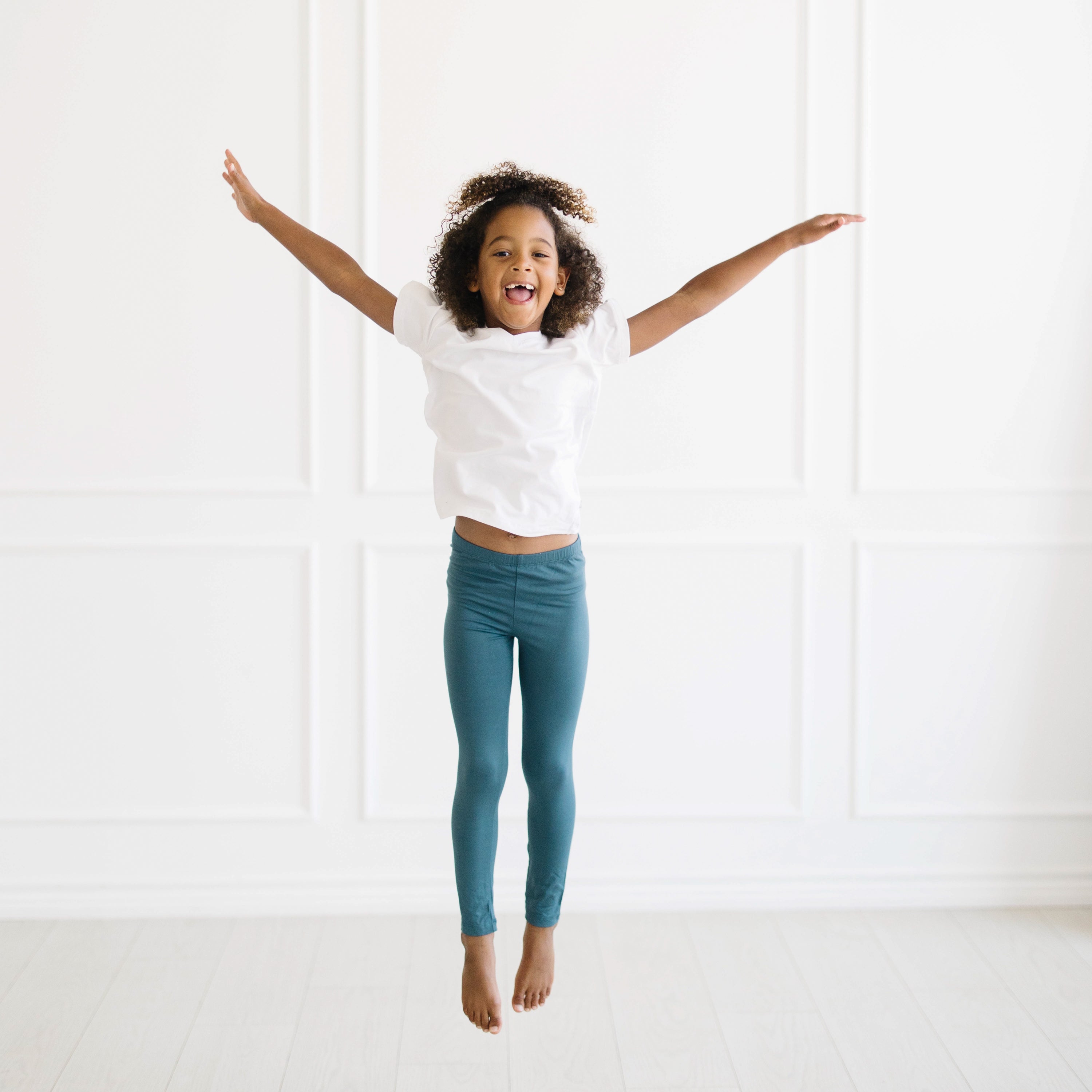 Young girl jumping in the air wearing the Toddler Leggings in Atlantic and Snow V-Neck