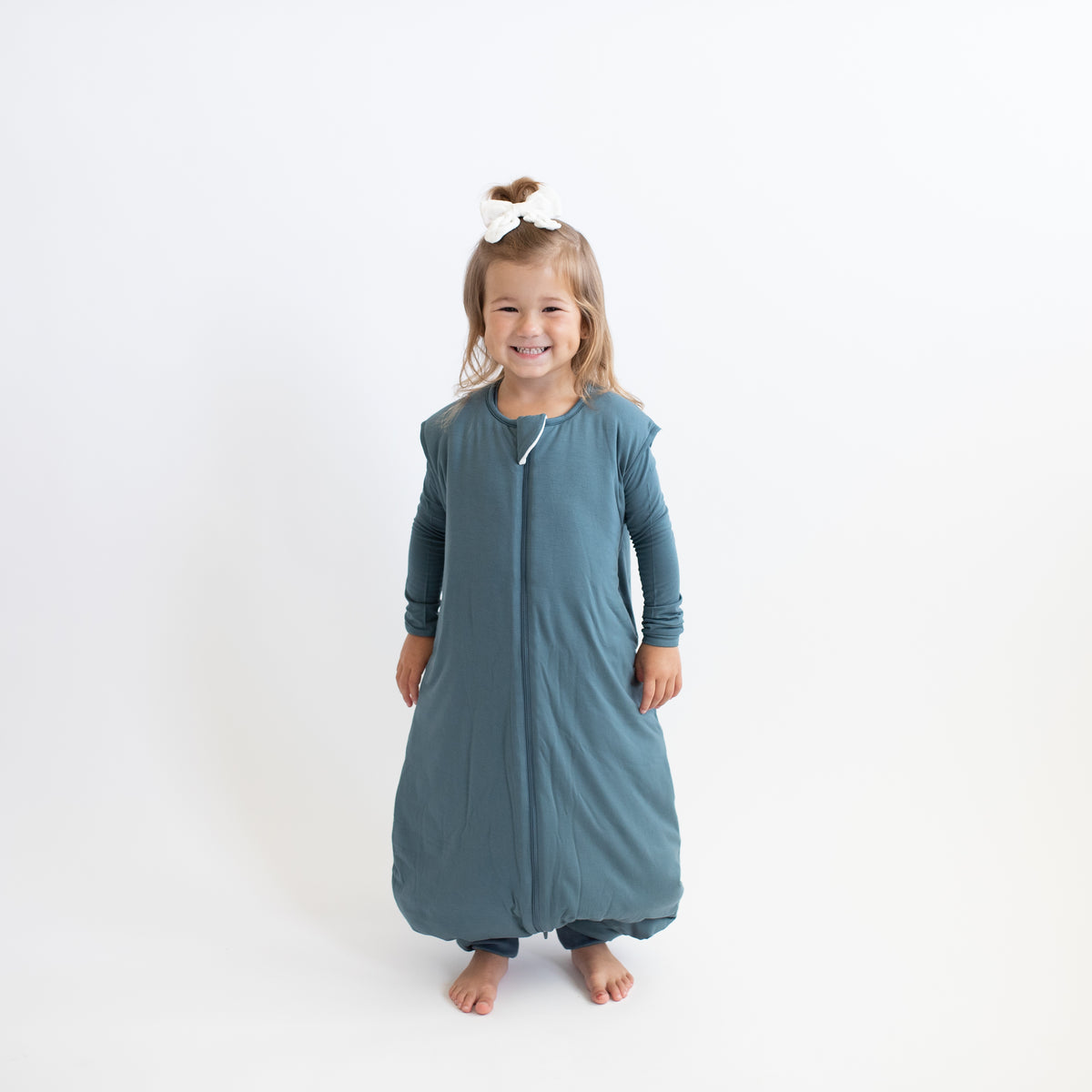Smiling girl wearing the Sleep Bag Walker in Atlantic 2.5 with matching long sleeve toddler pajamas on underneath