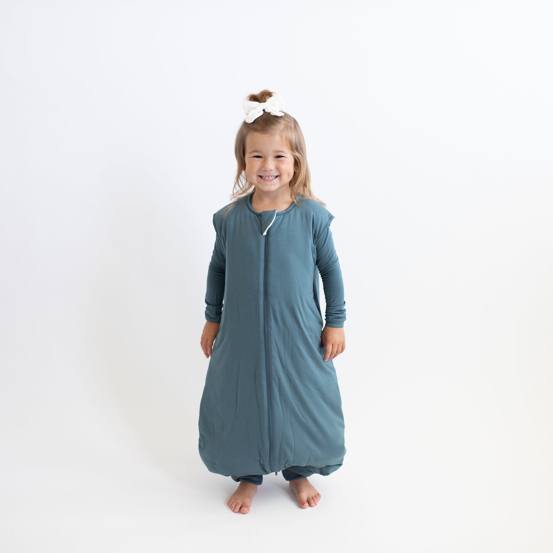 Smiling girl wearing the Sleep Bag Walker in Atlantic 2.5 with matching long sleeve toddler pajamas on underneath