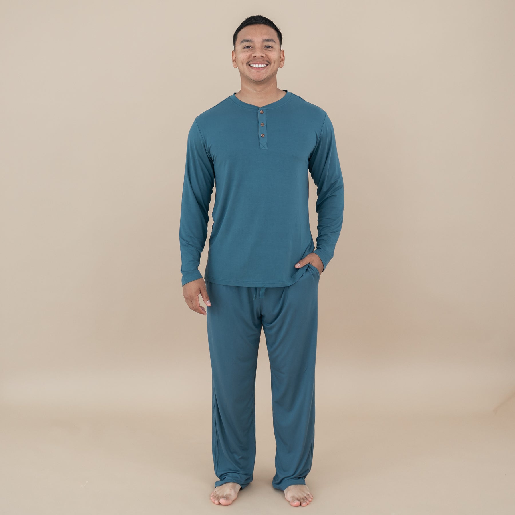 Smiling male model with hand in the pants pocket of the Men's Lounge Pants in Atlantic with matching Men's Long Sleeve Henley Tee