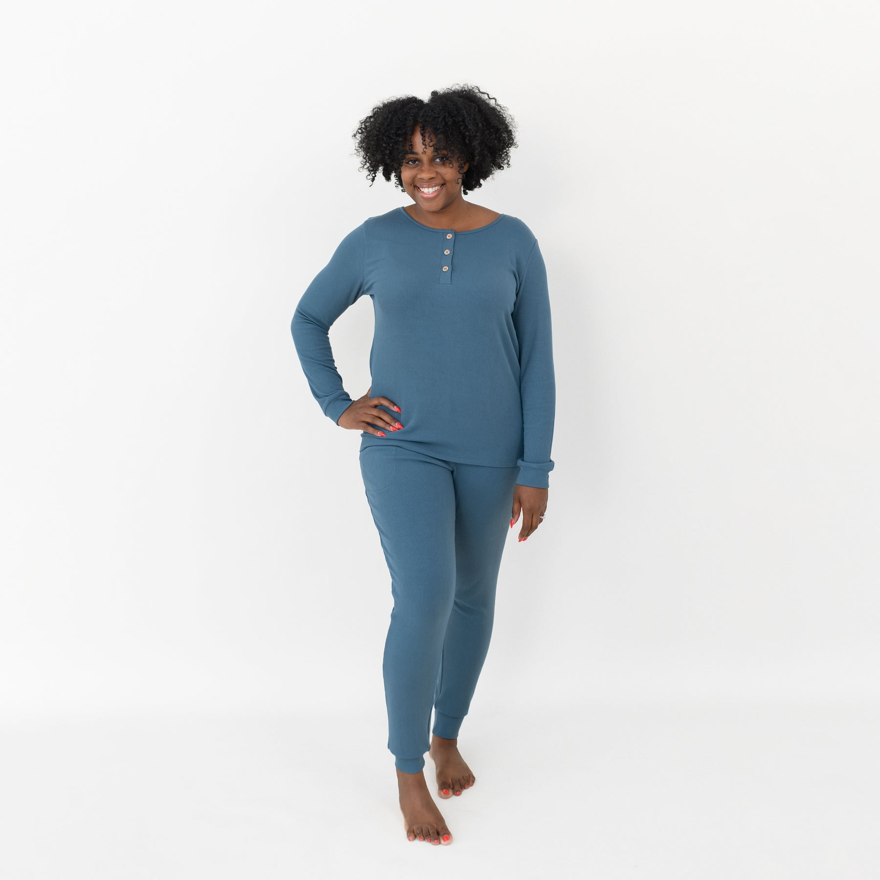 Smiling female model wearing the Women’s Ribbed Henley Set in Atlantic with one had on her hip in front of a white backdrop