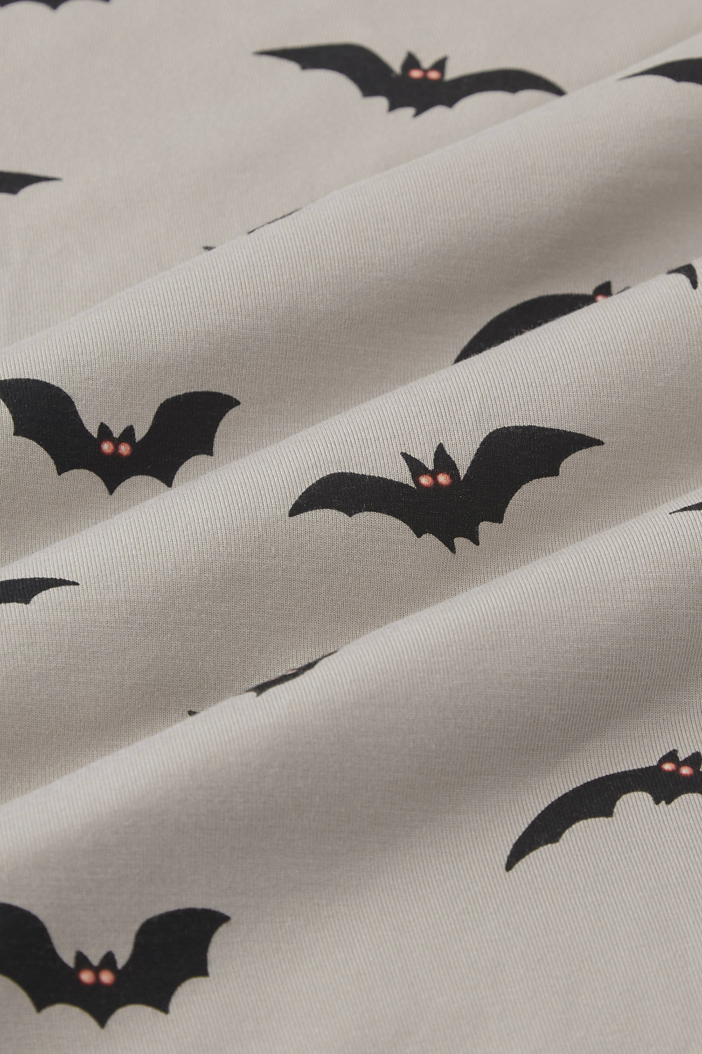 An all-over print featuring the silhouettes of various flying bats with orange eyes over a light tan background color called Khaki.