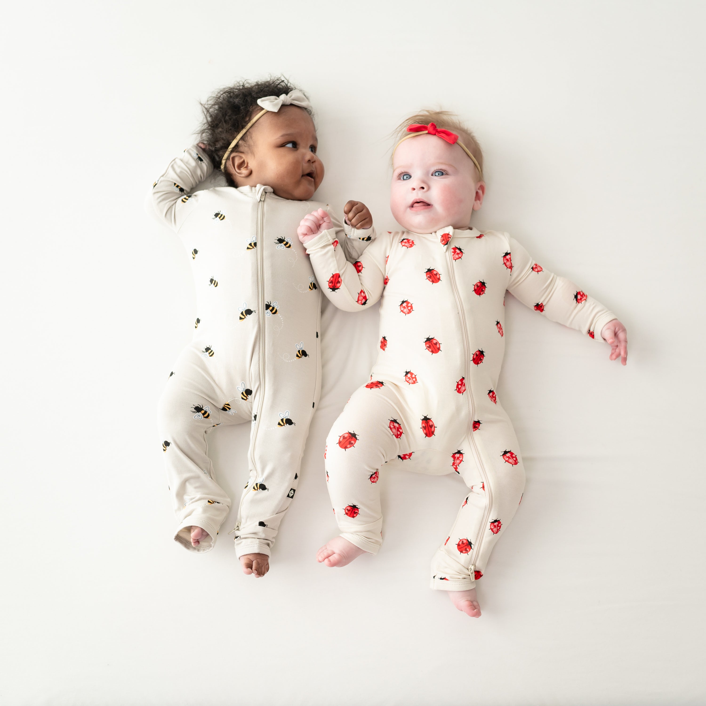 Two babies laying wearing zippered rompers in bee mine and love bug 