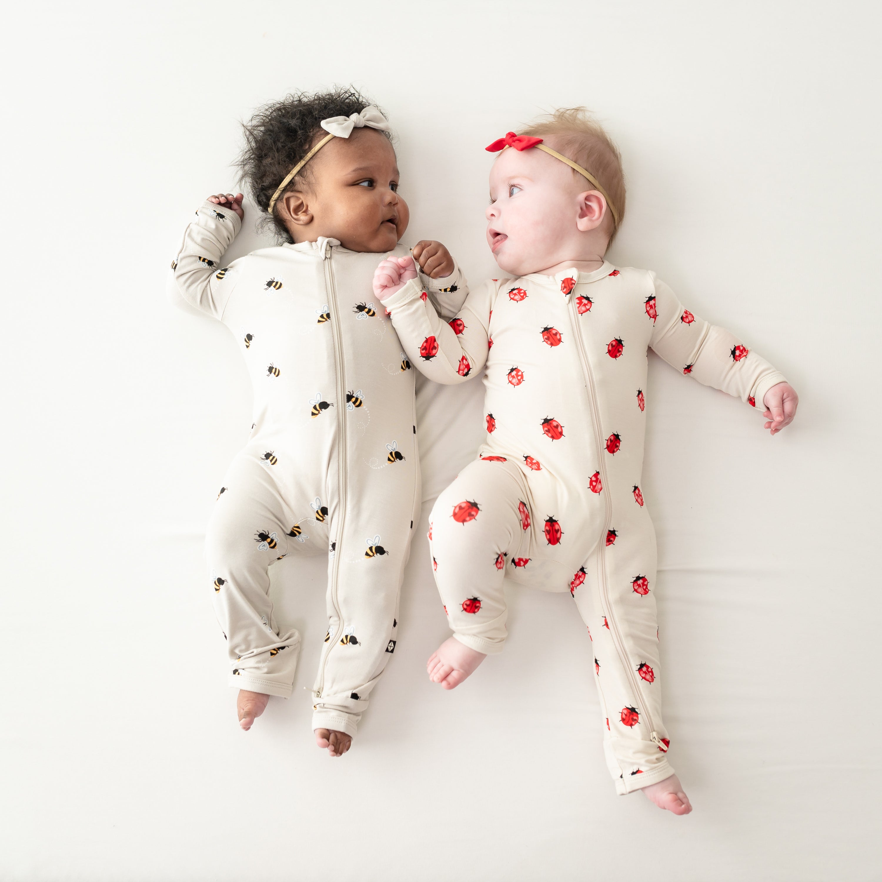 Two babies laying down wearing zippered rompers in Bee Mine and Love Bug