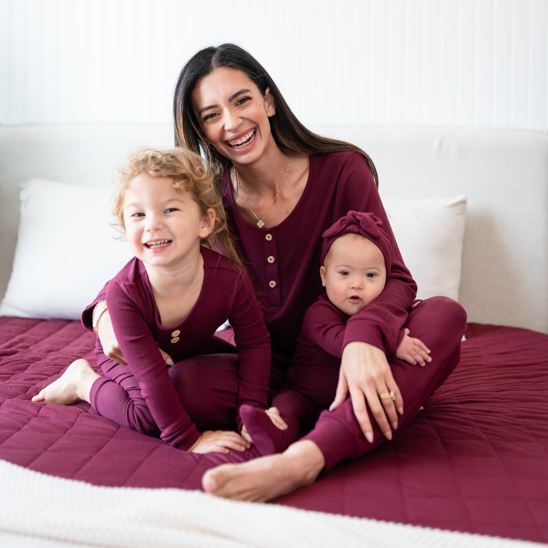 Family of three sitting on a bed wearing Ribbed Burgundy items