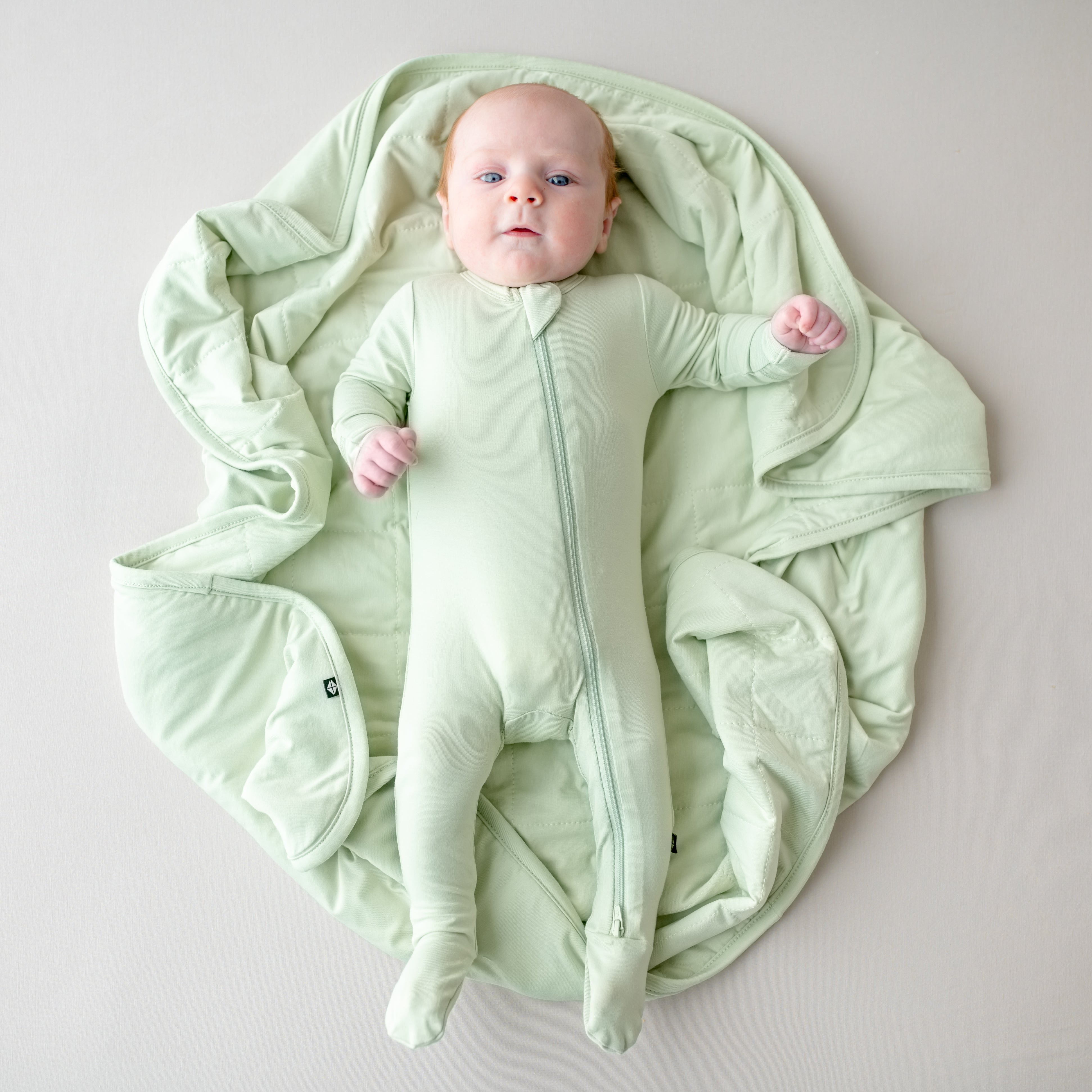 Baby in a light green footie laying on a matching green blanket