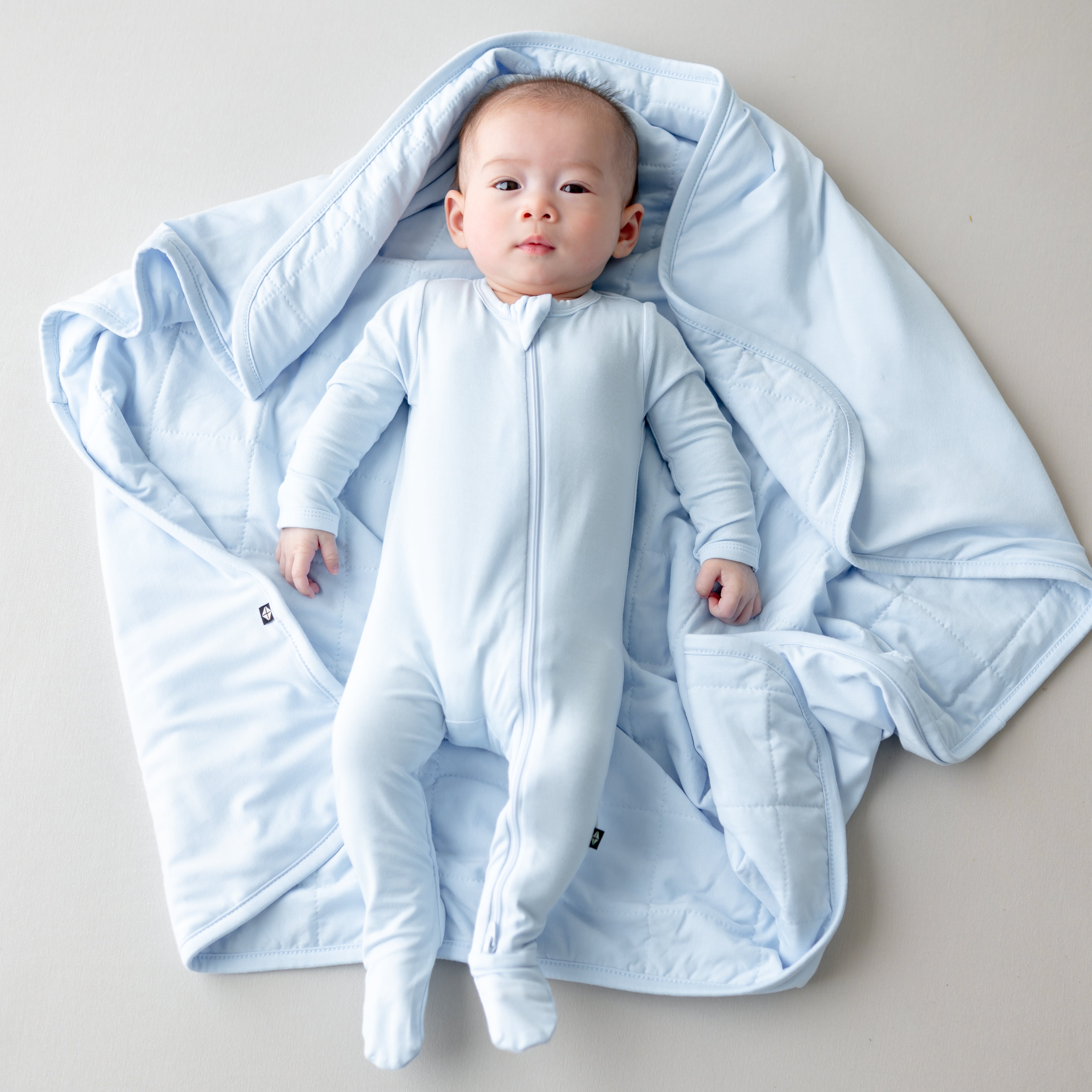Baby in a blue footie laying on a baby blanket 