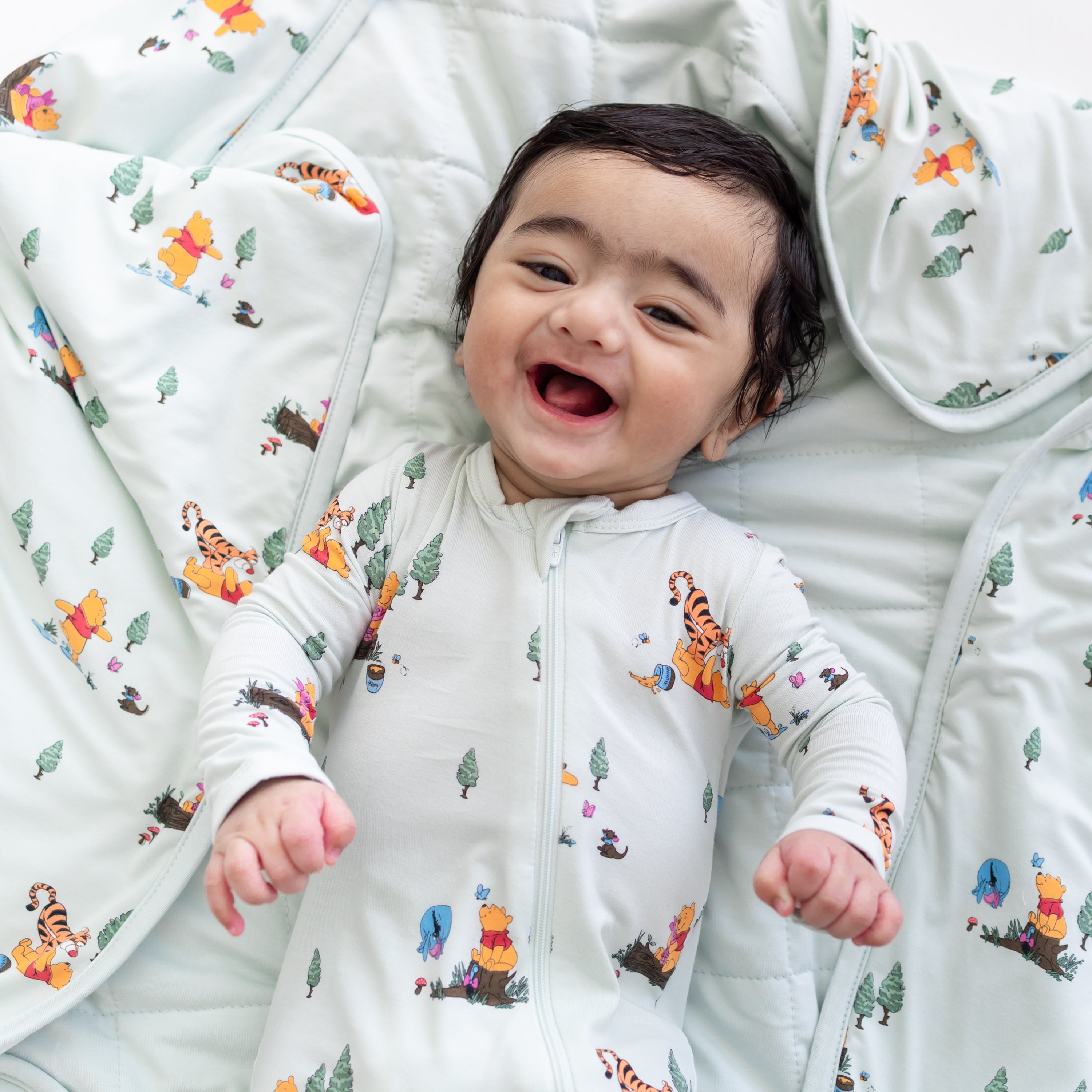 Close up of smiling infant laying on a Baby Blanket in Winnie the Pooh Hundred Acre Wood wearing a matching zippered romper