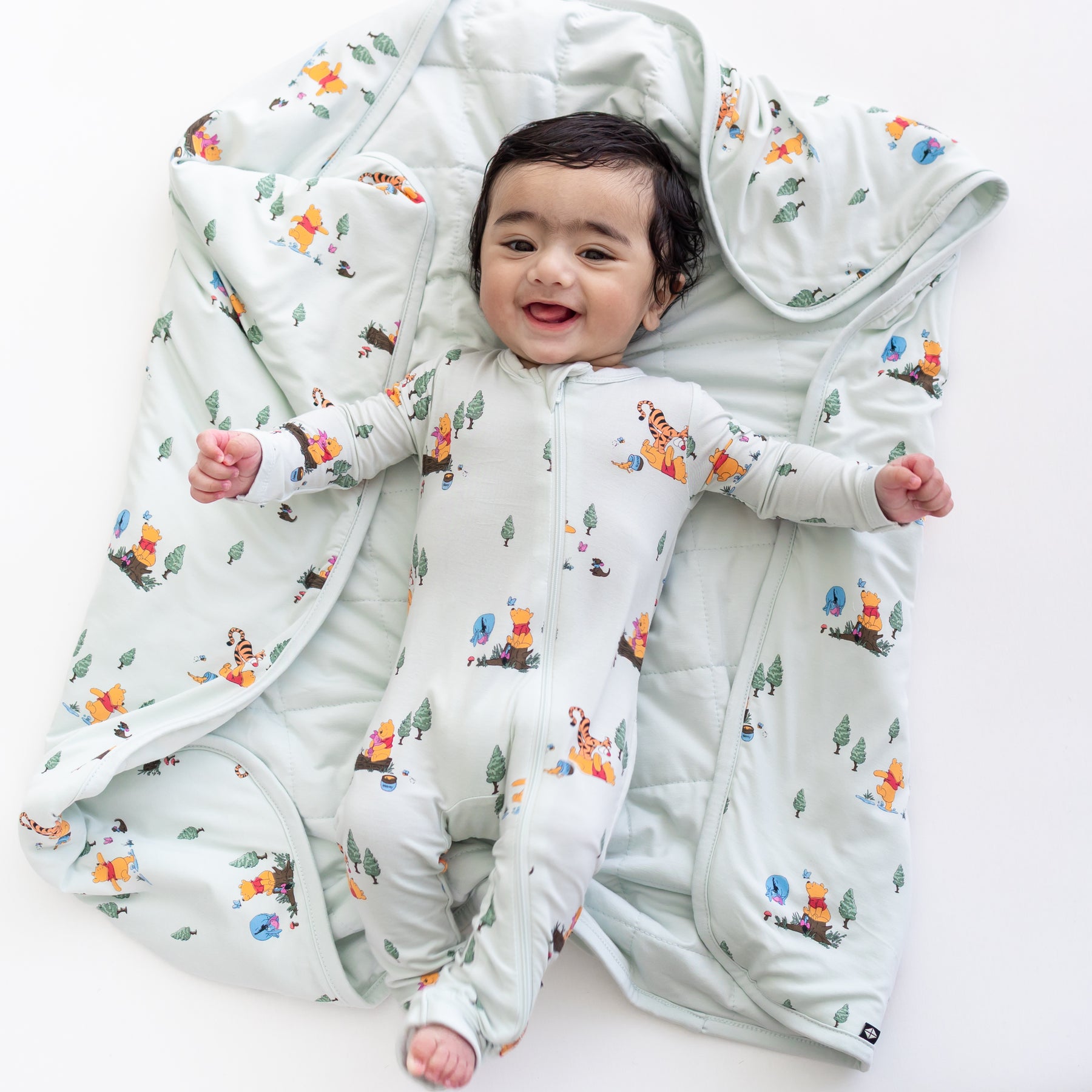 Infant laying on the Baby Blanket in Winnie the Pooh Hundred Acre Wood wearing a matching a zippered romper