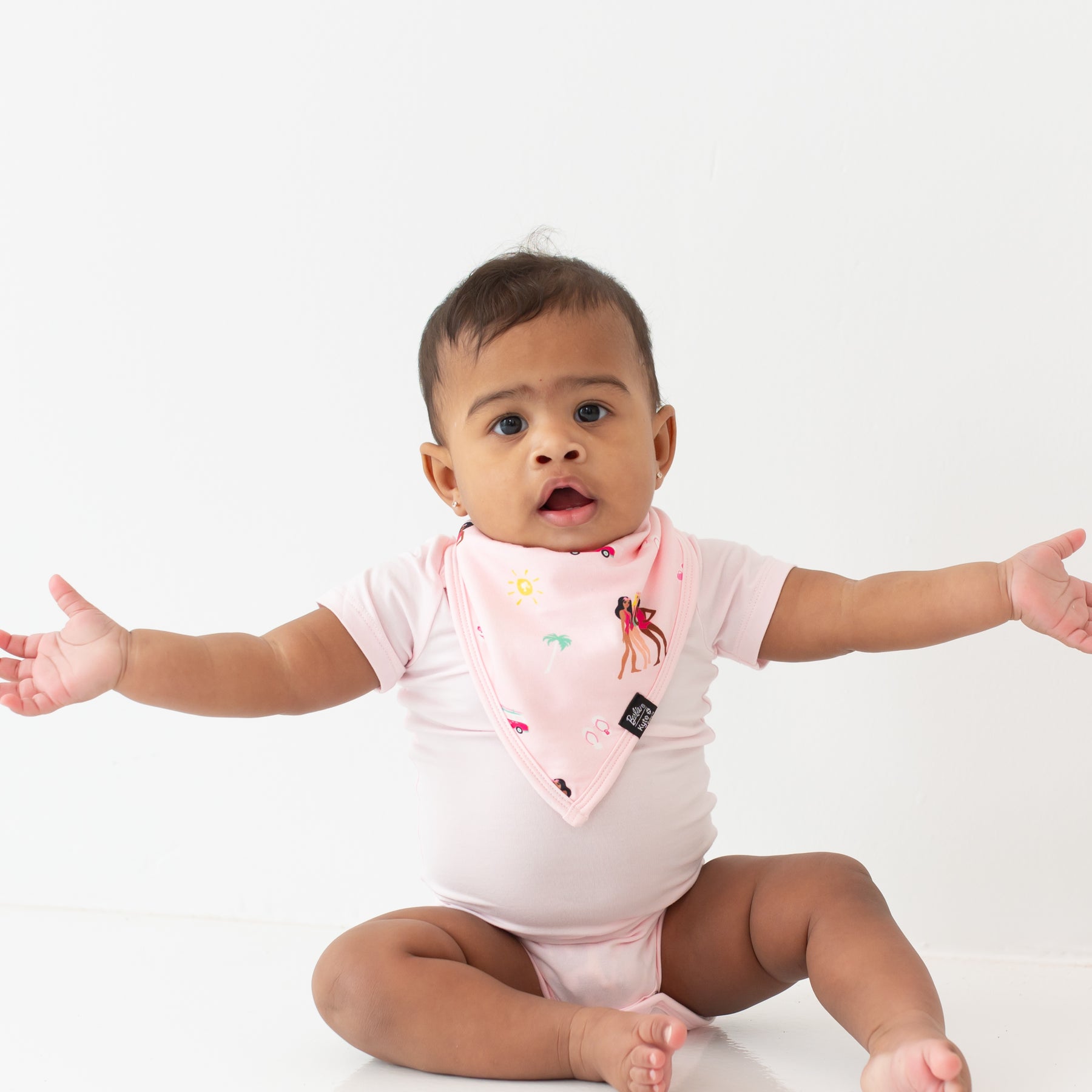 Baby sitting wearing Baby wearing Bib in Barbie™ Beach and Sakura bodysuit