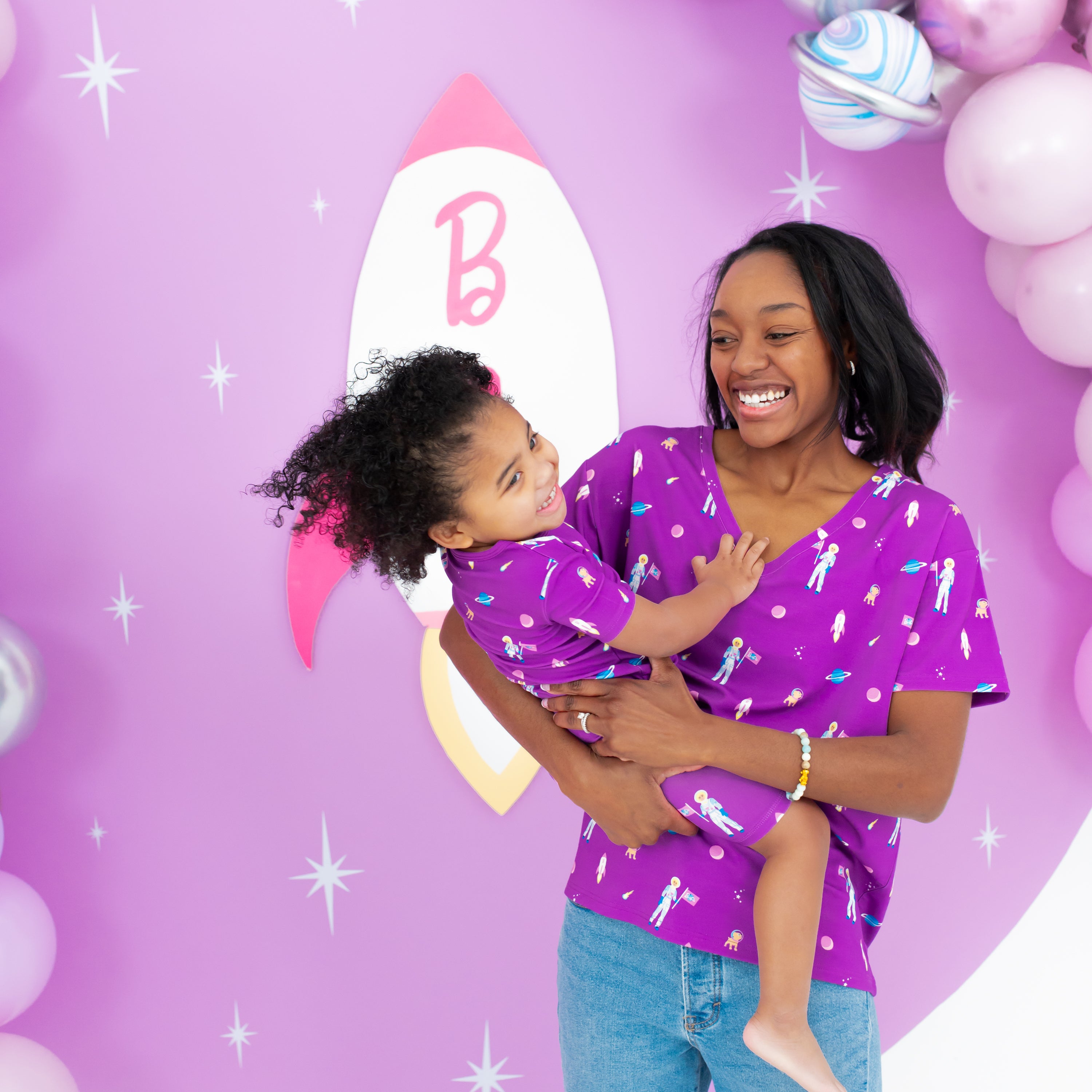 Toddler smiling wearing Short Sleeve Pajamas in Barbie™ Astronaut being held by mom  