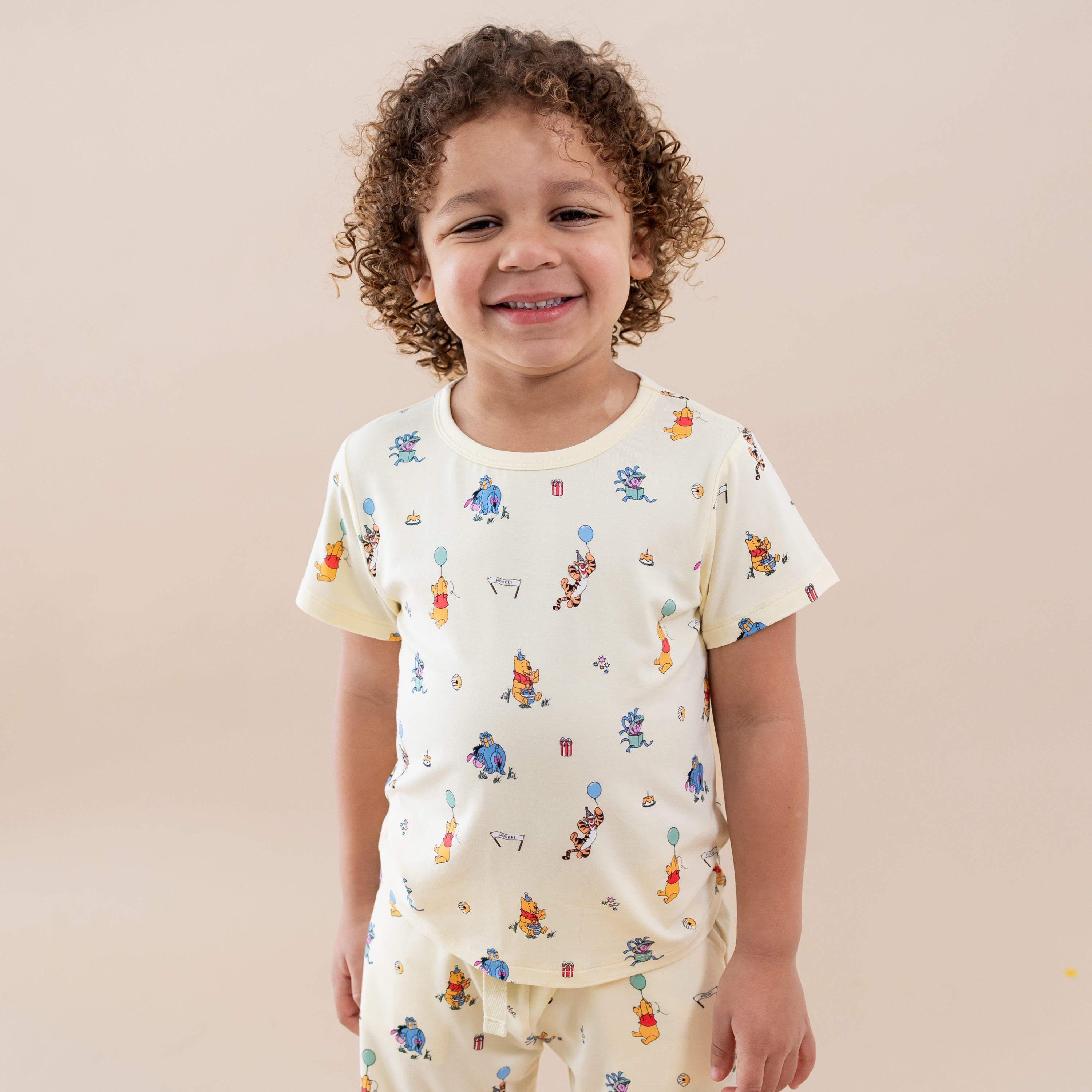 Smiling boy wearing the Toddler Basic Tee in Winnie the Pooh Celebration with matching shorts
