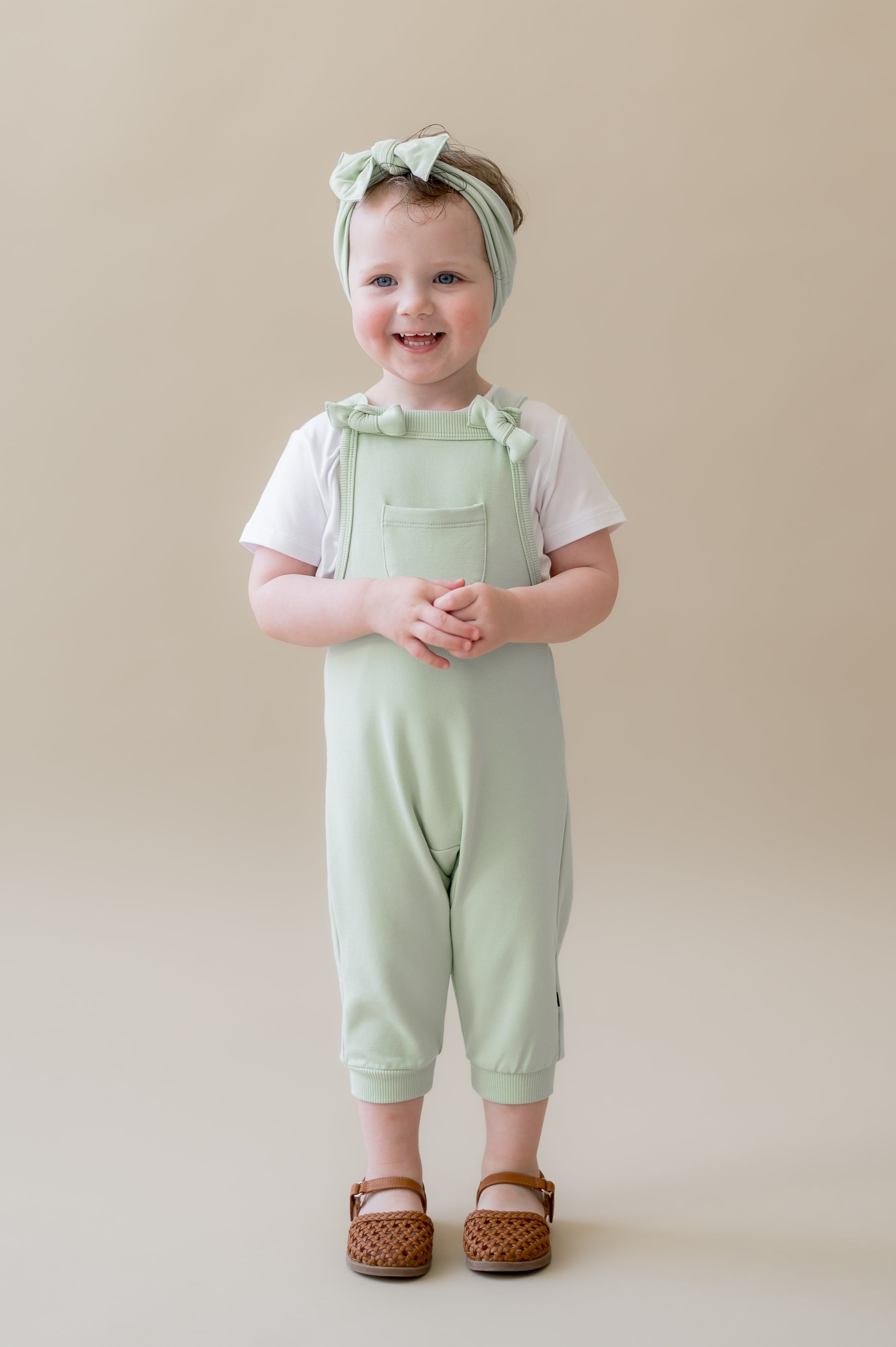 Young girl wearing the Overall in Basil with a white shirt on underneath