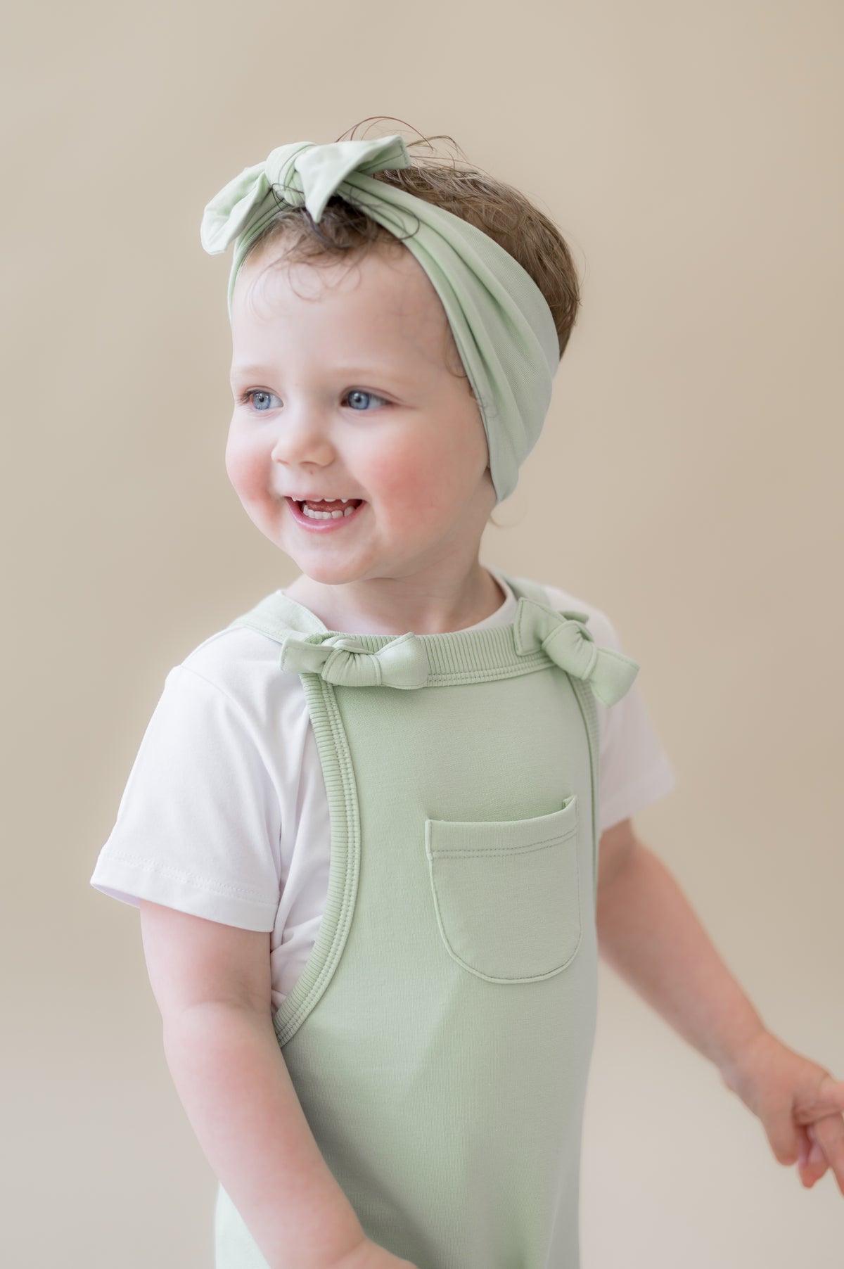 Close up of a young girl wearing the Overall in Basil showing the front pocket