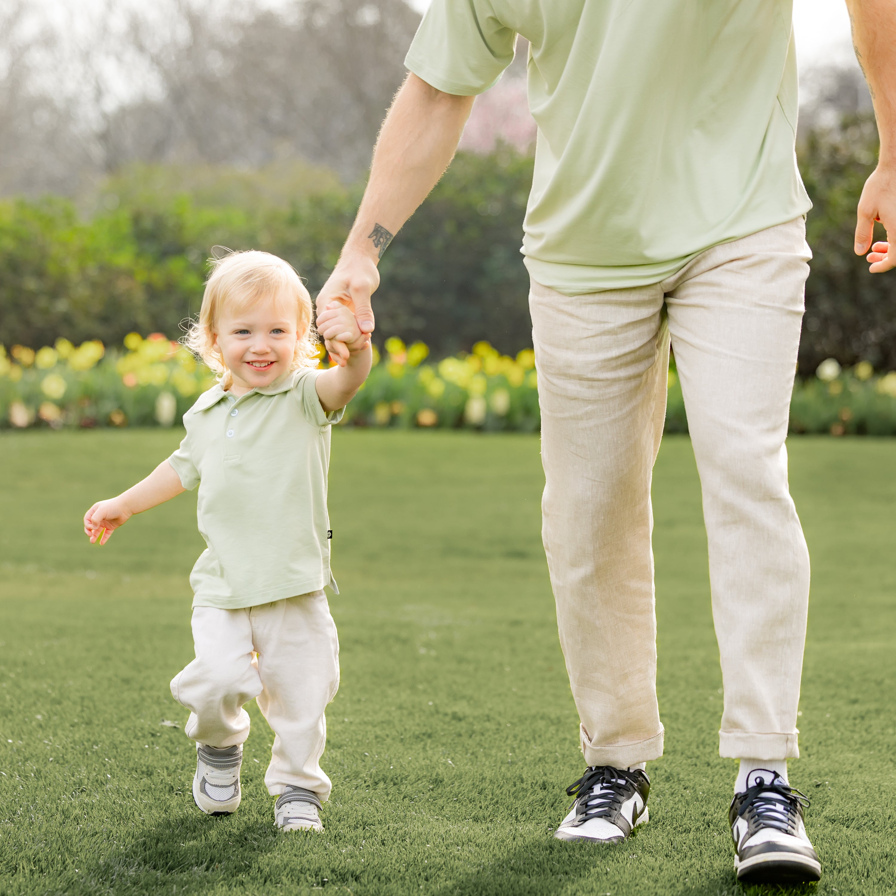 Young boy walking wearing the Toddler Short Sleeve Polo in Basil holding his father's hand