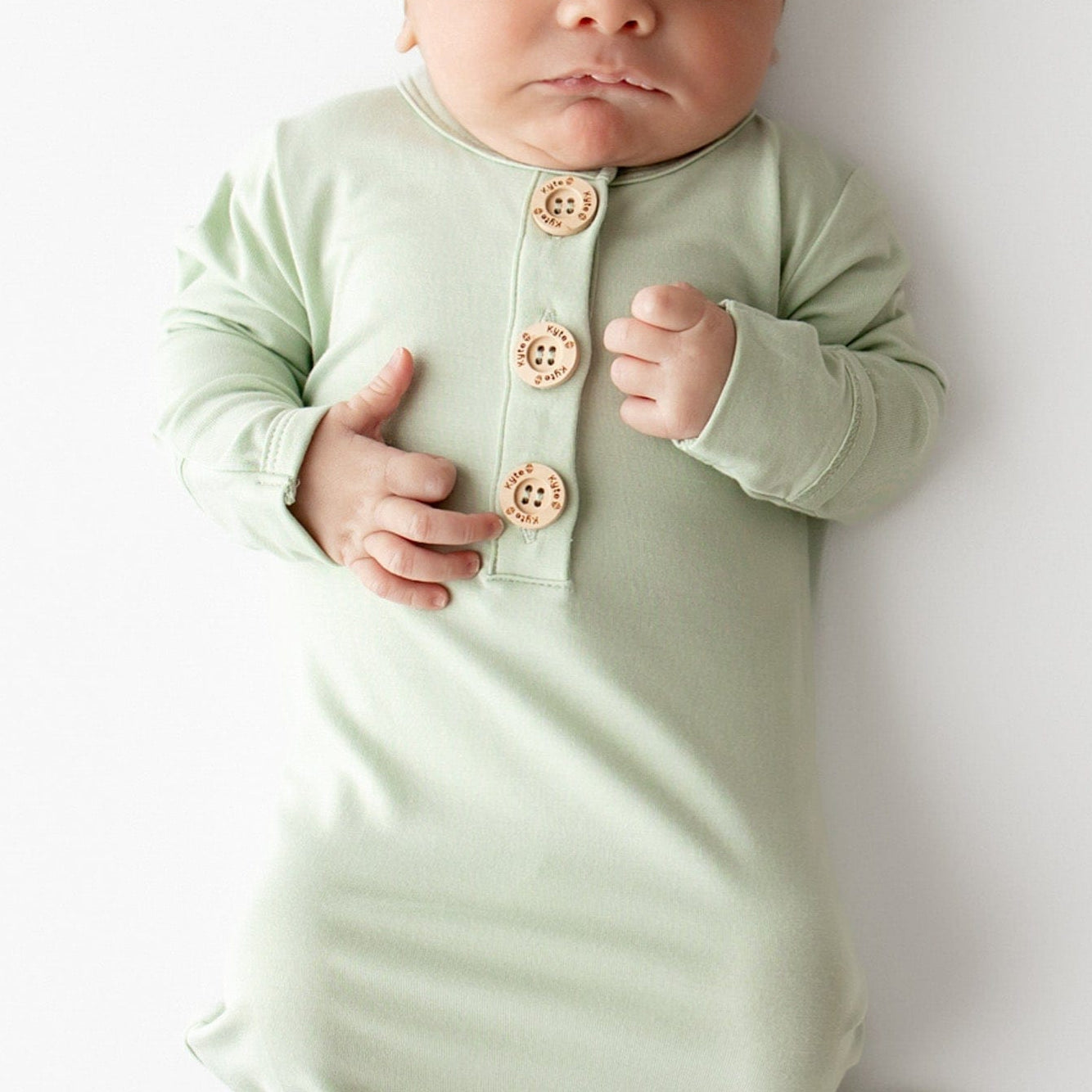 Baby wearing a light green knotted gown and cap set