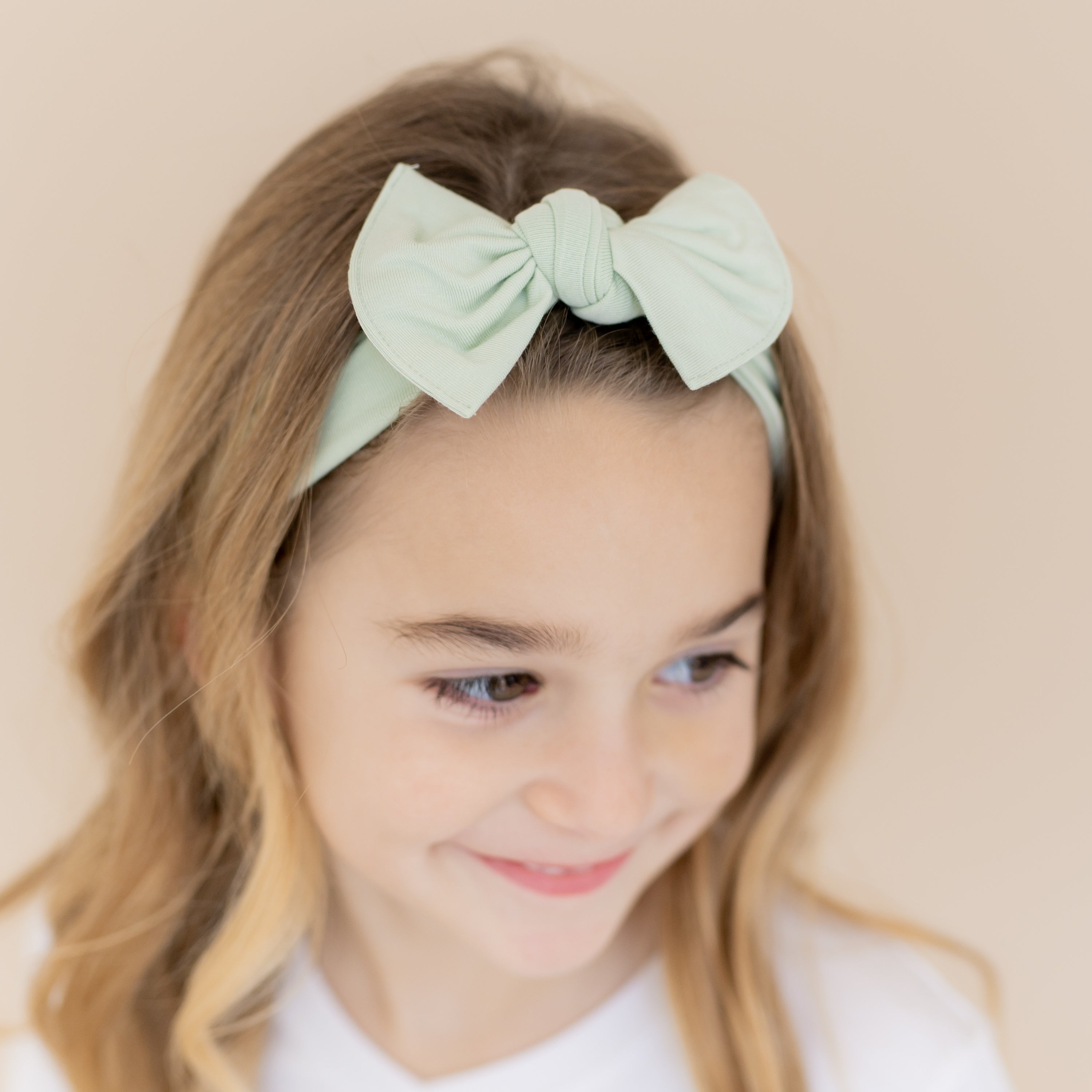 Close up of the Knotted Bow Headband in Basil shown on a young girl