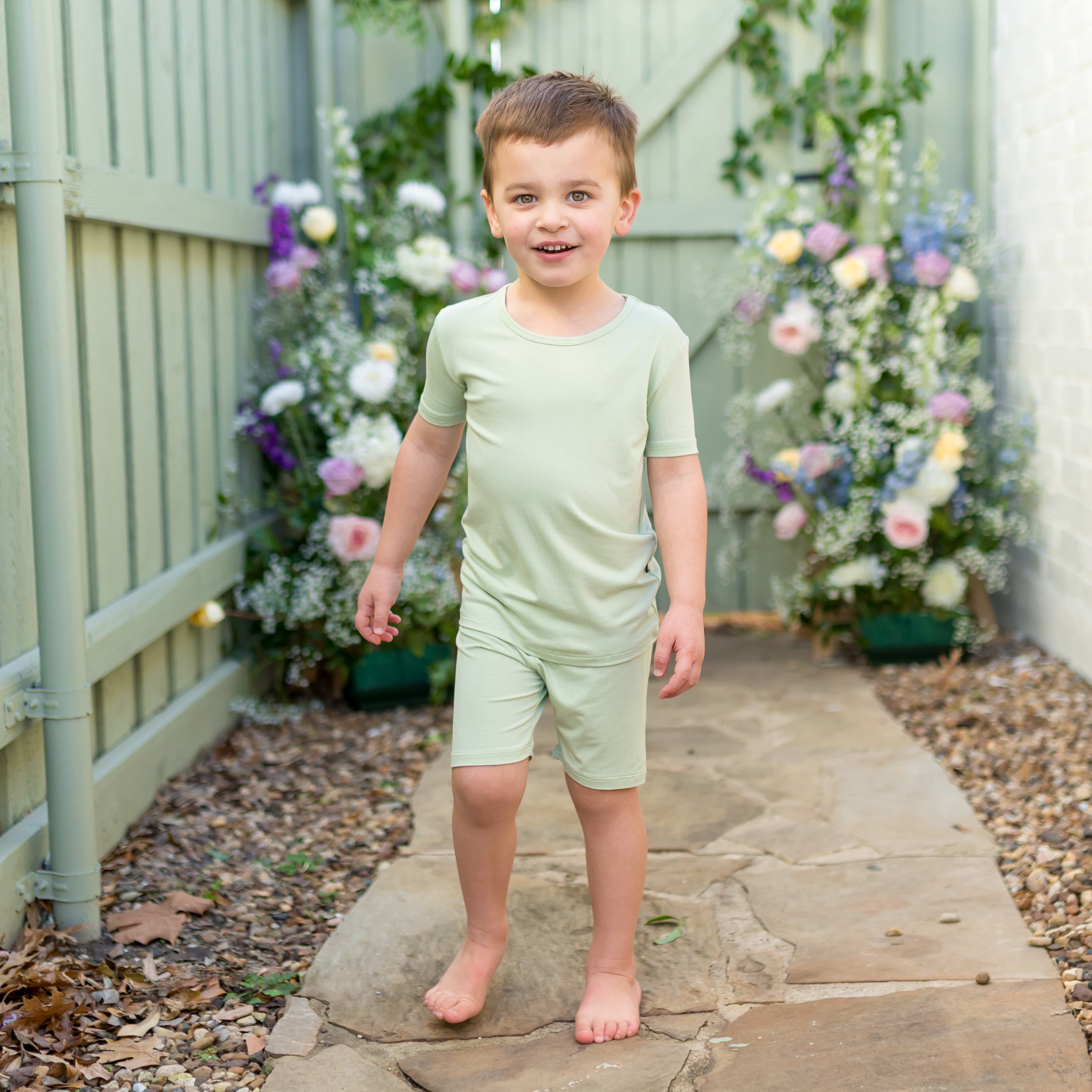 Young boy walking on a stone path wearing the soft and breathable Short Sleeve Pajamas in Basil