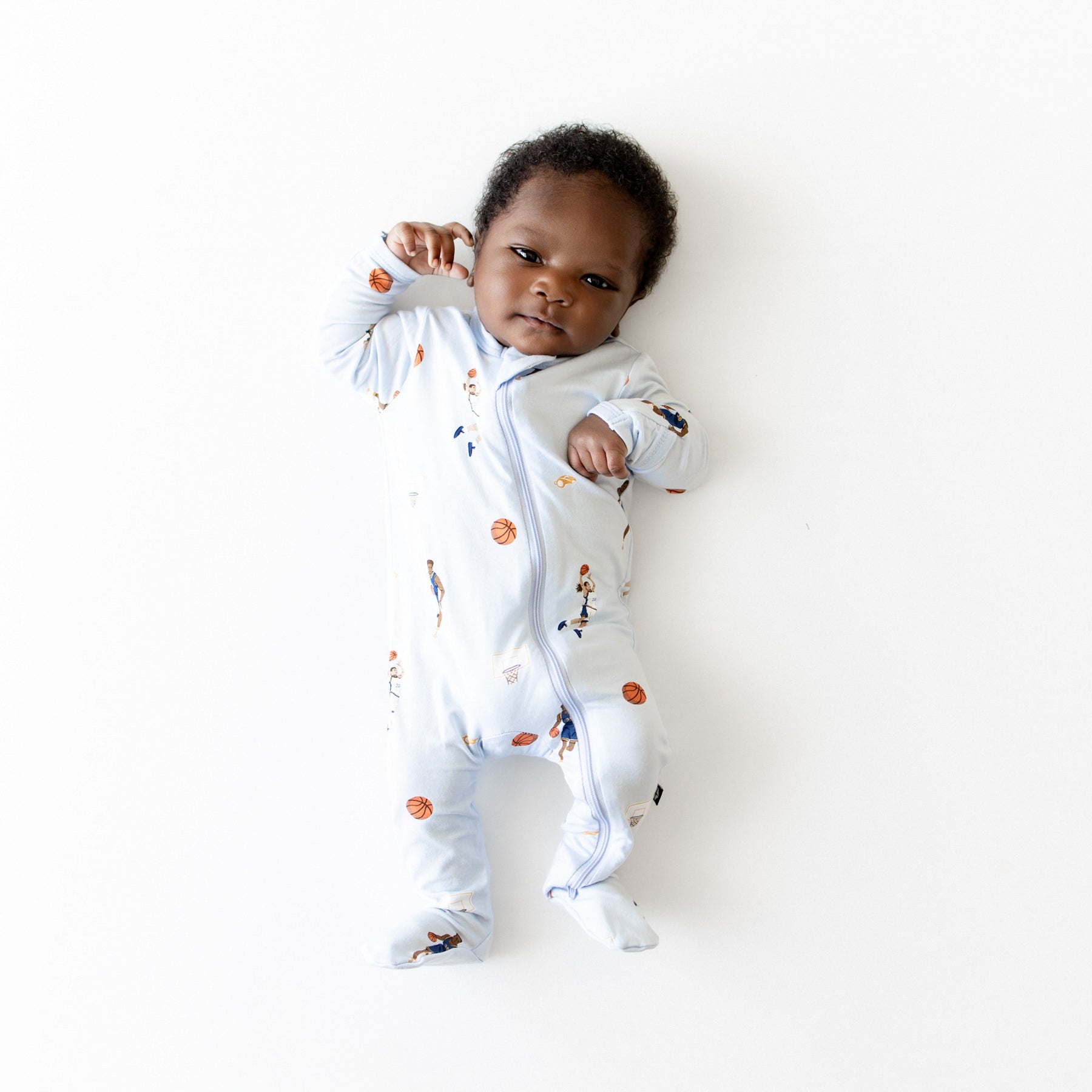 Young infant laying a white neutral background wearing the Zippered Footie in Basketball