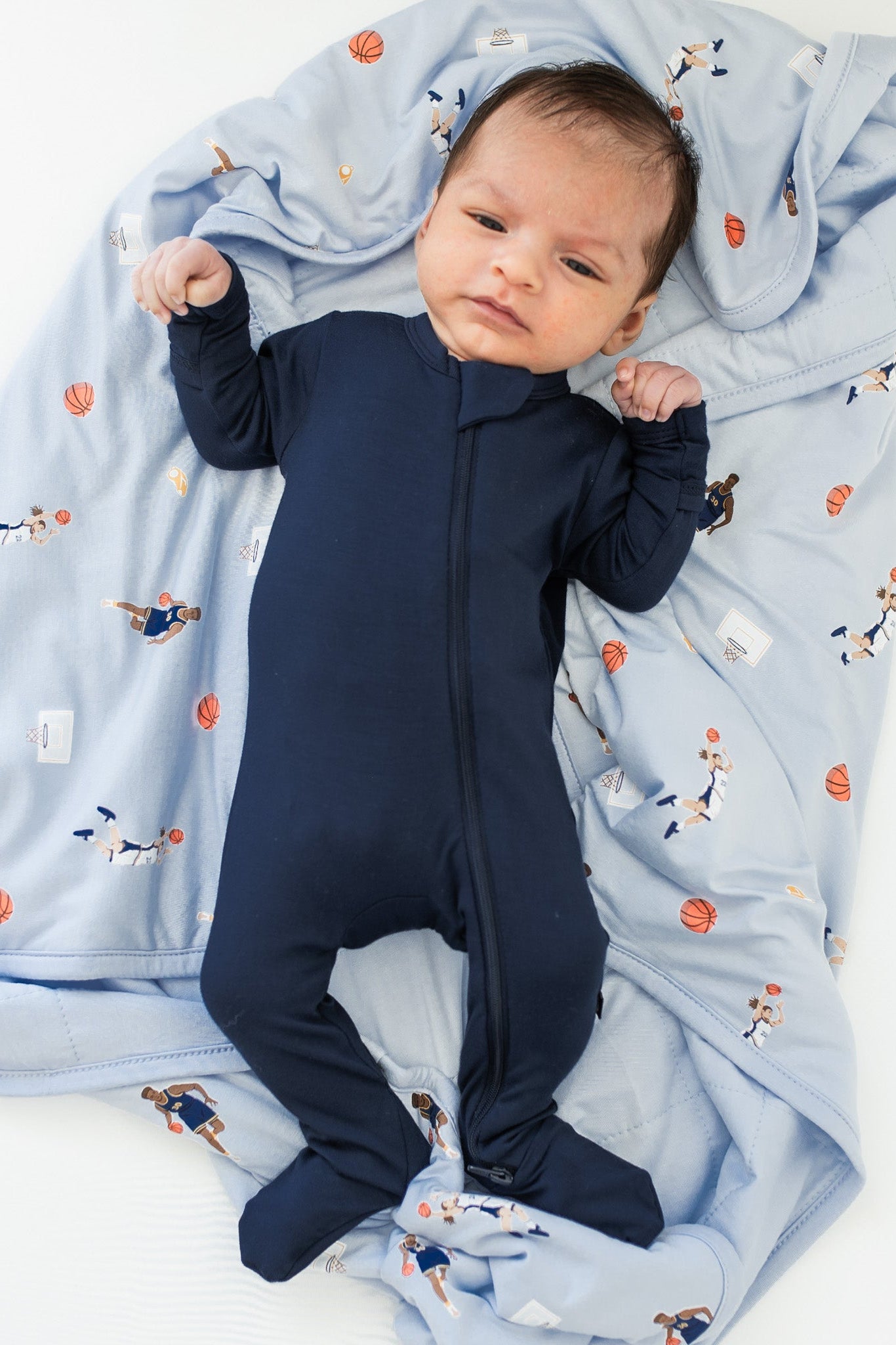 Infant laying on a Baby Blanket in Basketball wearing a Navy zippered footie
