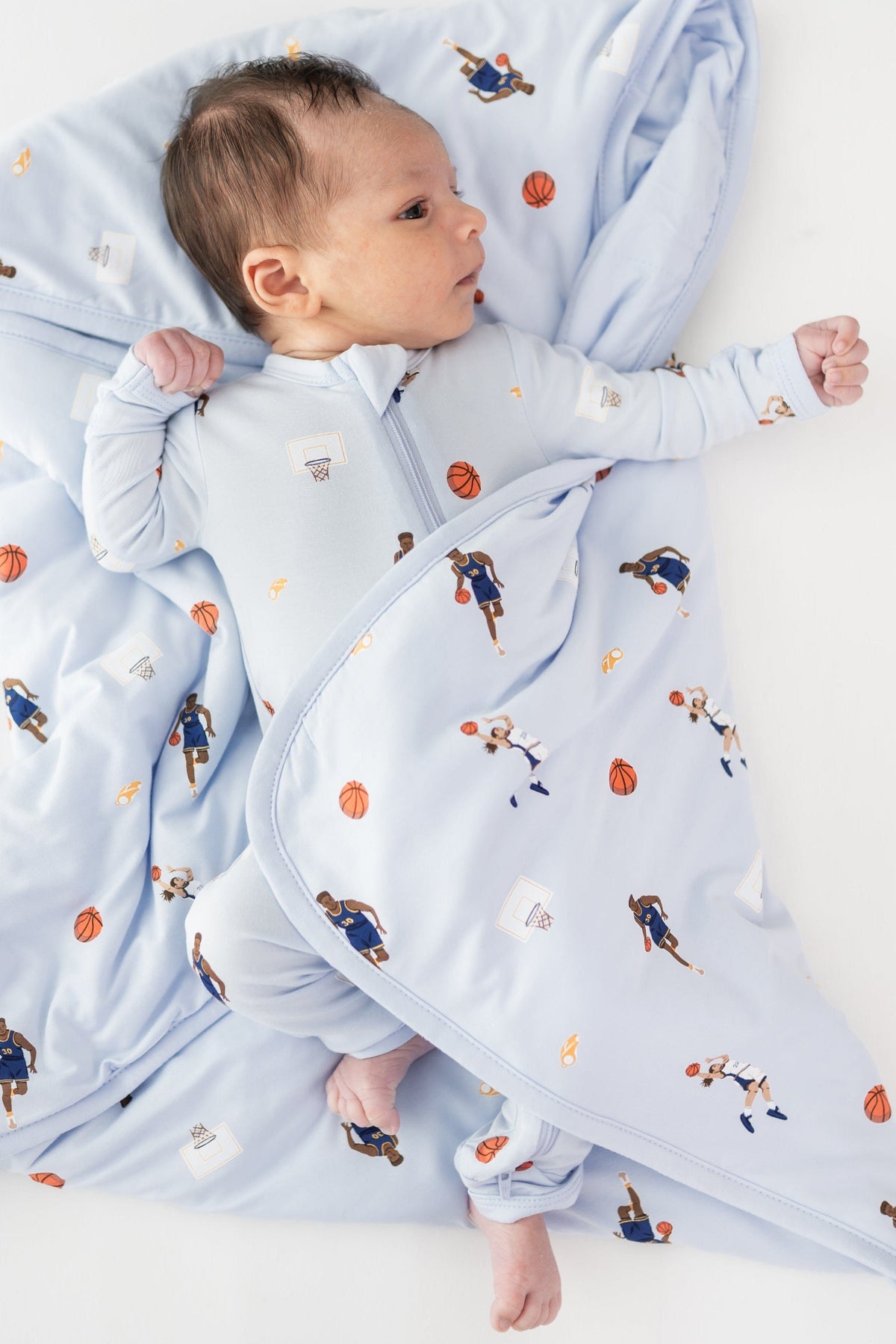 Infant laying on a Baby Blanket in Basketball wearing a matching zippered romper