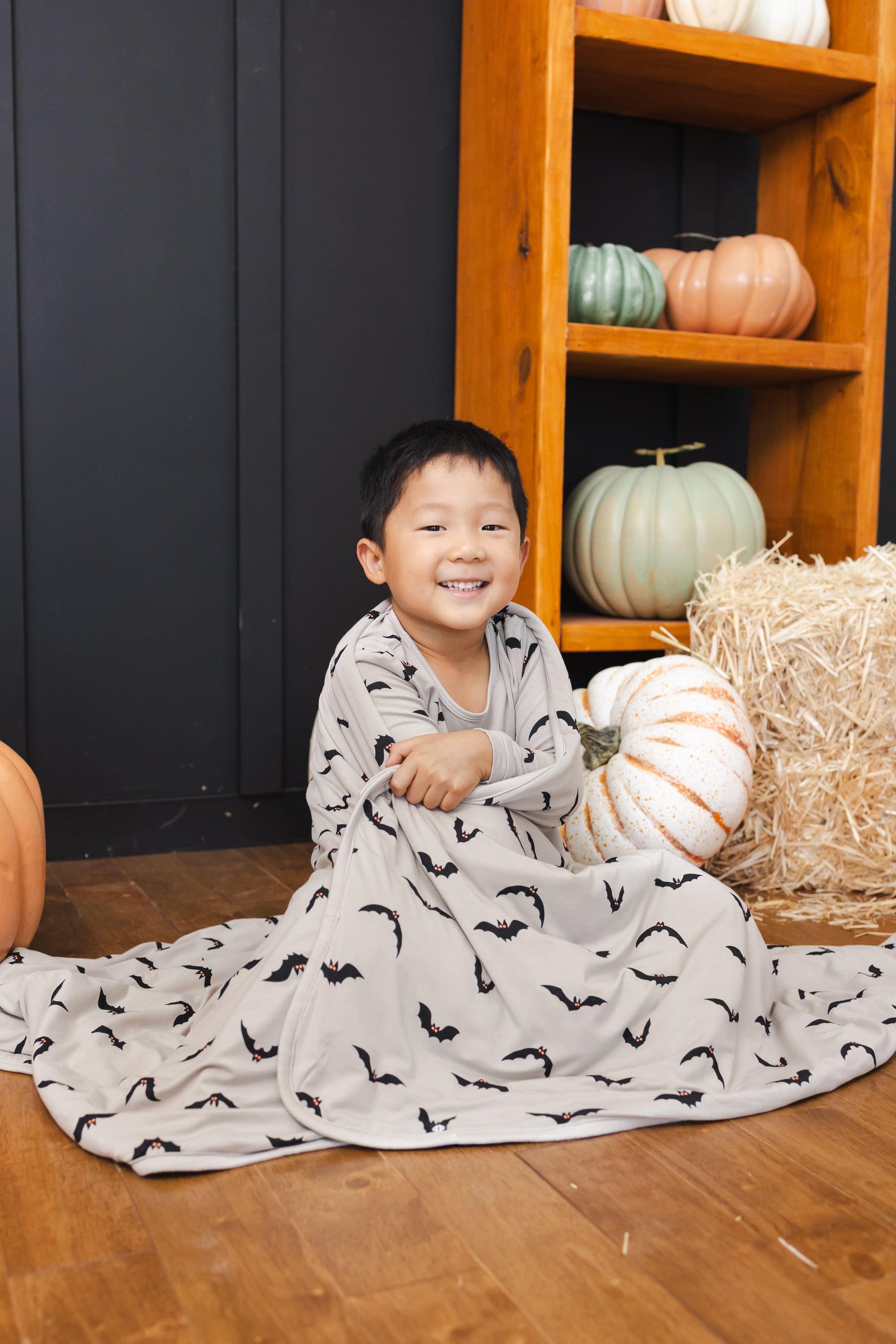 Boy wrapped in a Toddler Blanket in Bats 1.0 print sitting in a room with pumpkin props all around him