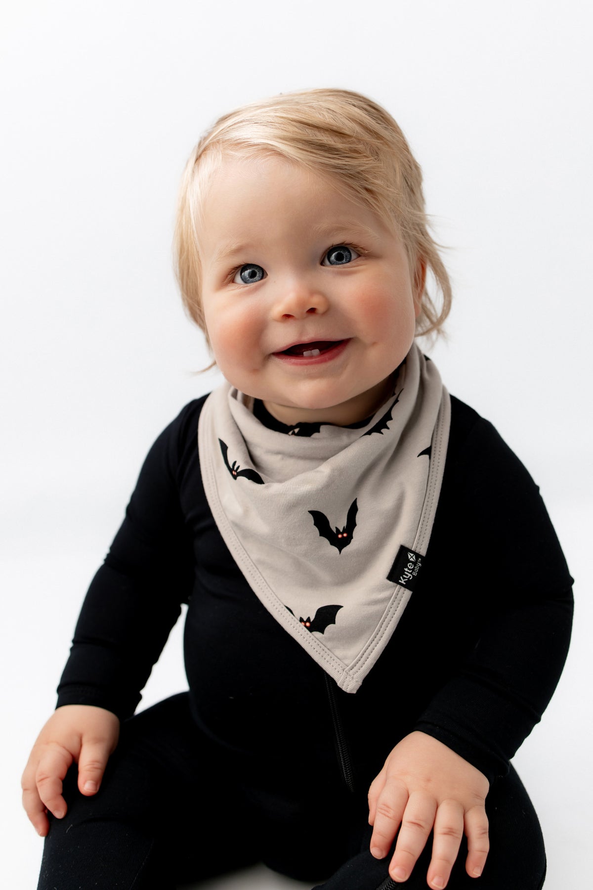 Baby smiling in Bib in Bats print over black romper sitting on a white background