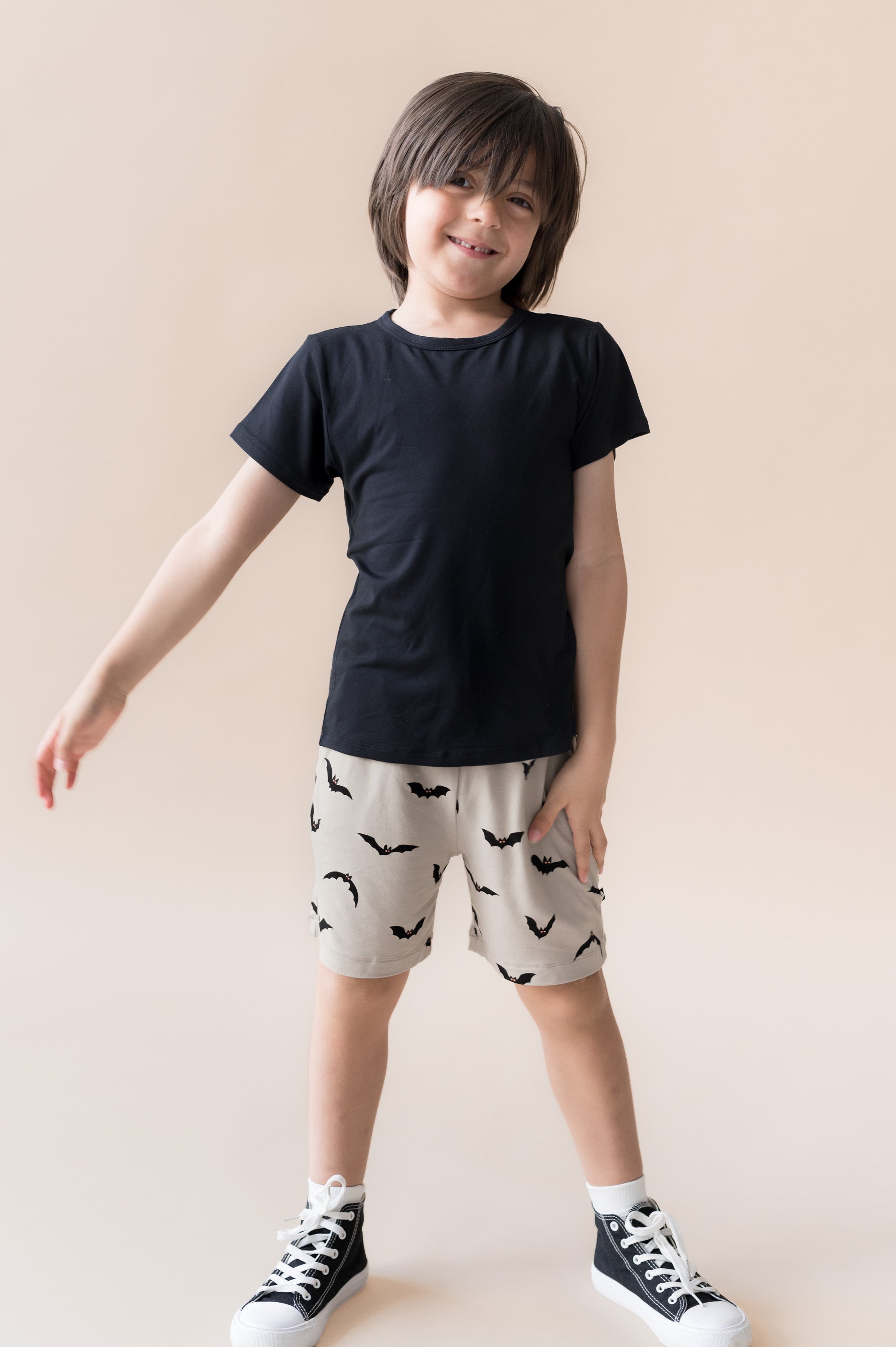Boy wearing Drawstring Short in Bats print under black T-shirt and shoes on a beige background