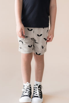 Toddler wearing Drawstring Short in Bats print under black T-shirt and shoes on a beige background