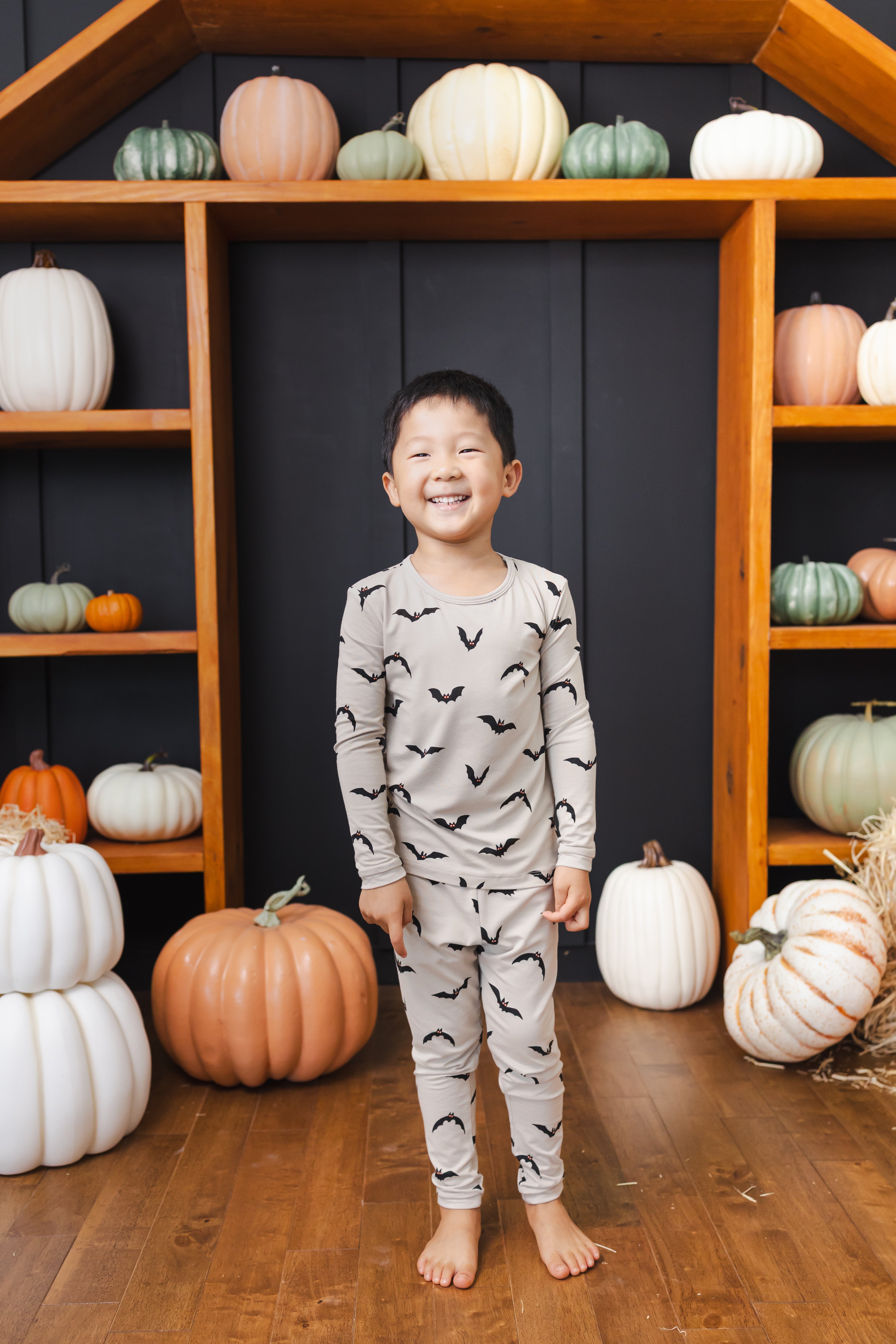 Boy wearing Long Sleeve Pajamas in Bats print standing in front of pumpkin decorations