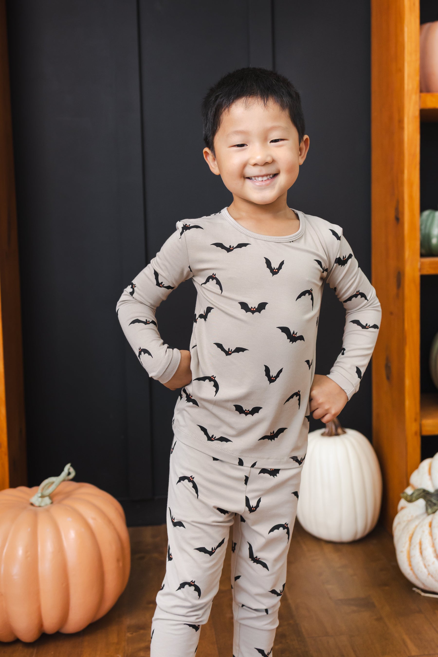 Boy posing in Long Sleeve Pajamas in Bats print standing in front of pumpkin decorations