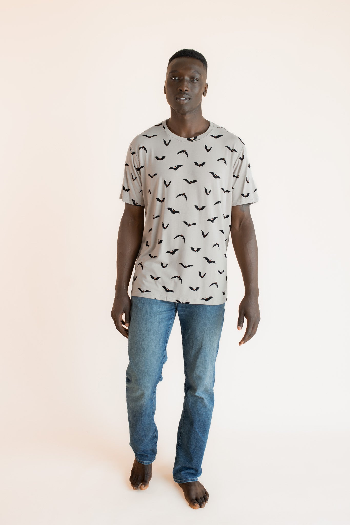 Modal posing in Men's Crew Neck Tee in Bats print over blue jeans on a beige background