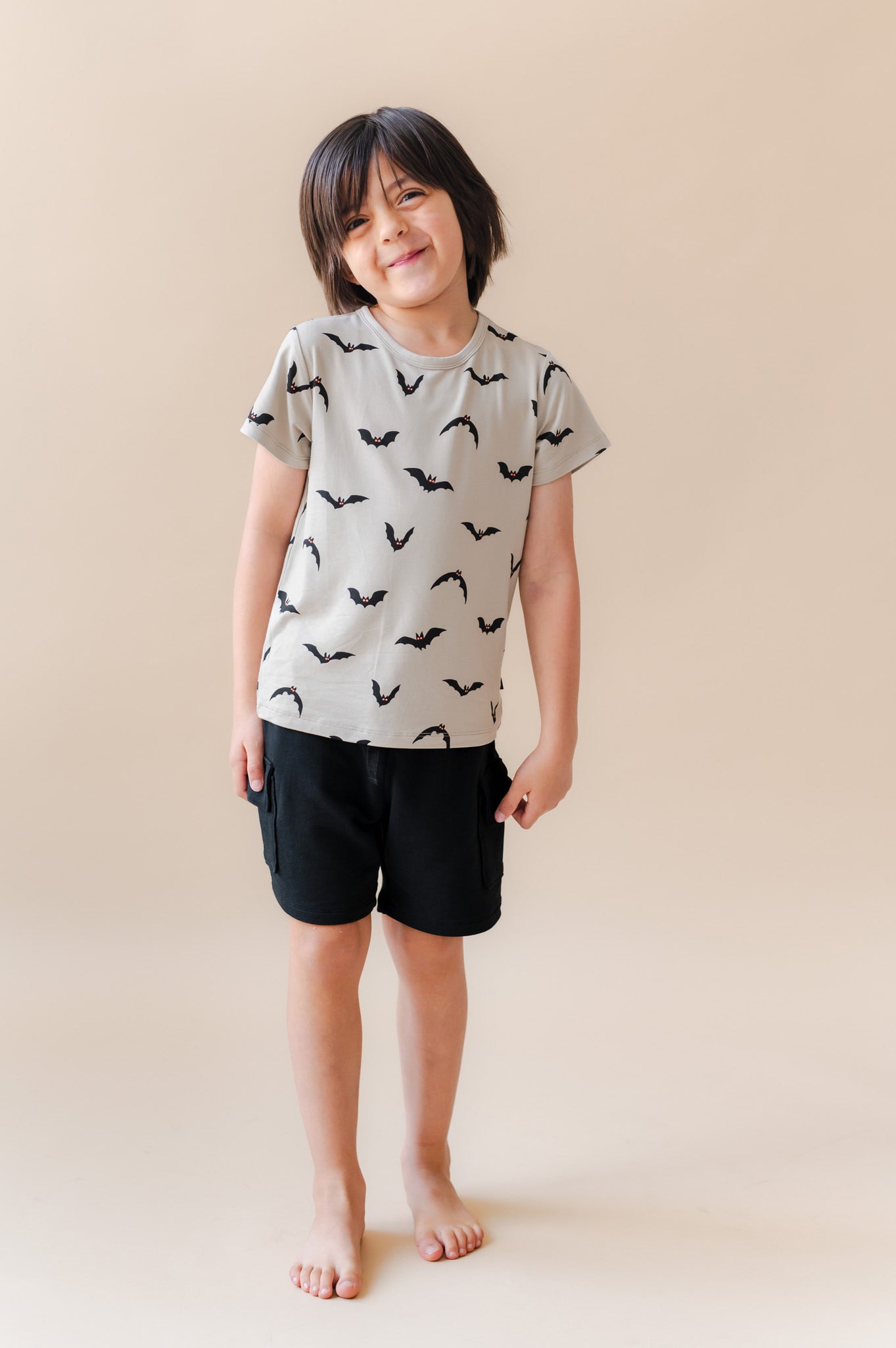 Boy posing in Toddler Basic Tee in Bats print over black shorts on a beige background