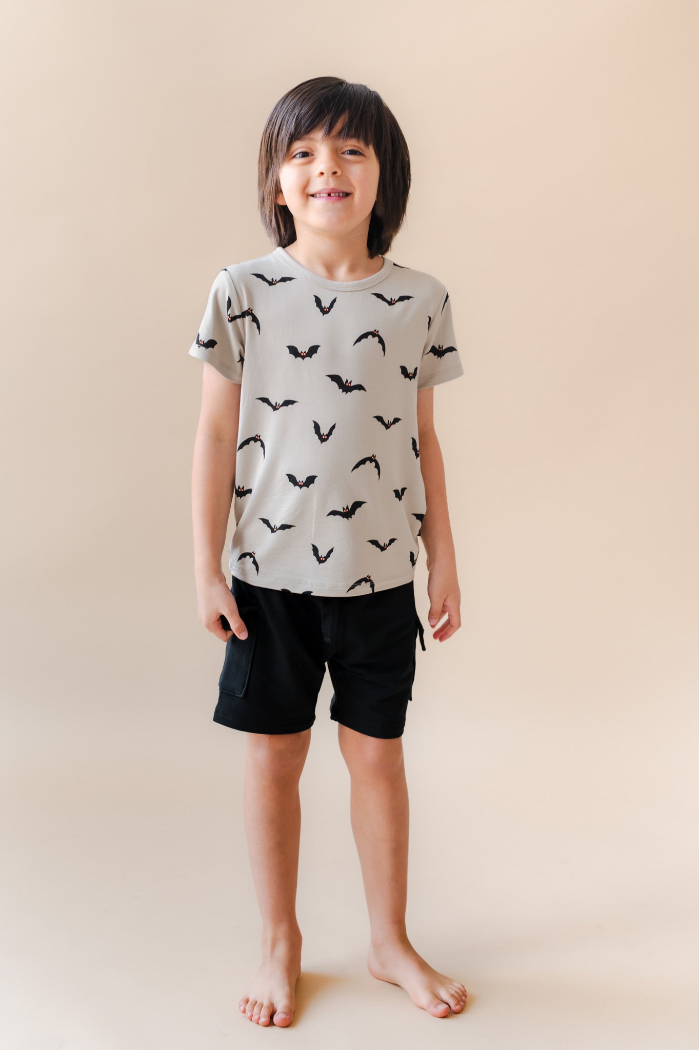 Boy wearing Toddler Basic Tee in Bats print over black shorts on a beige background